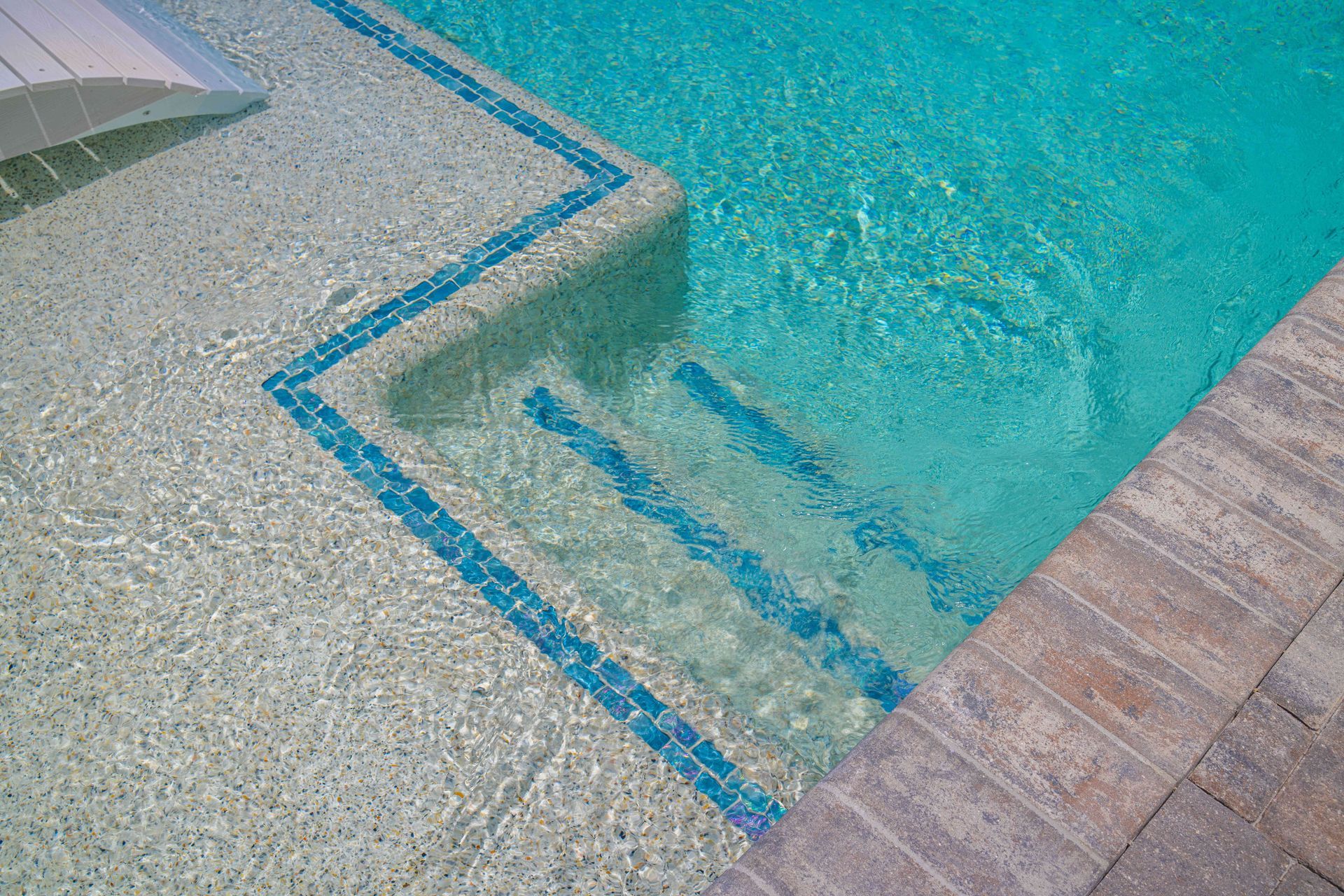 Pool steps with blue tile trim descending into clear turquoise water.