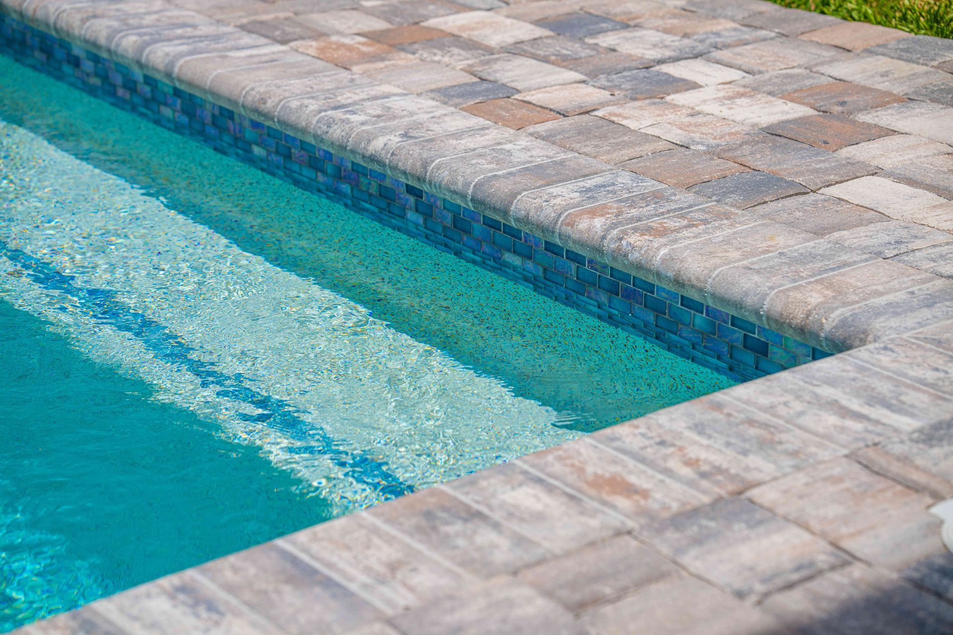 Tiled swimming pool edge with blue water and mosaic coping stones