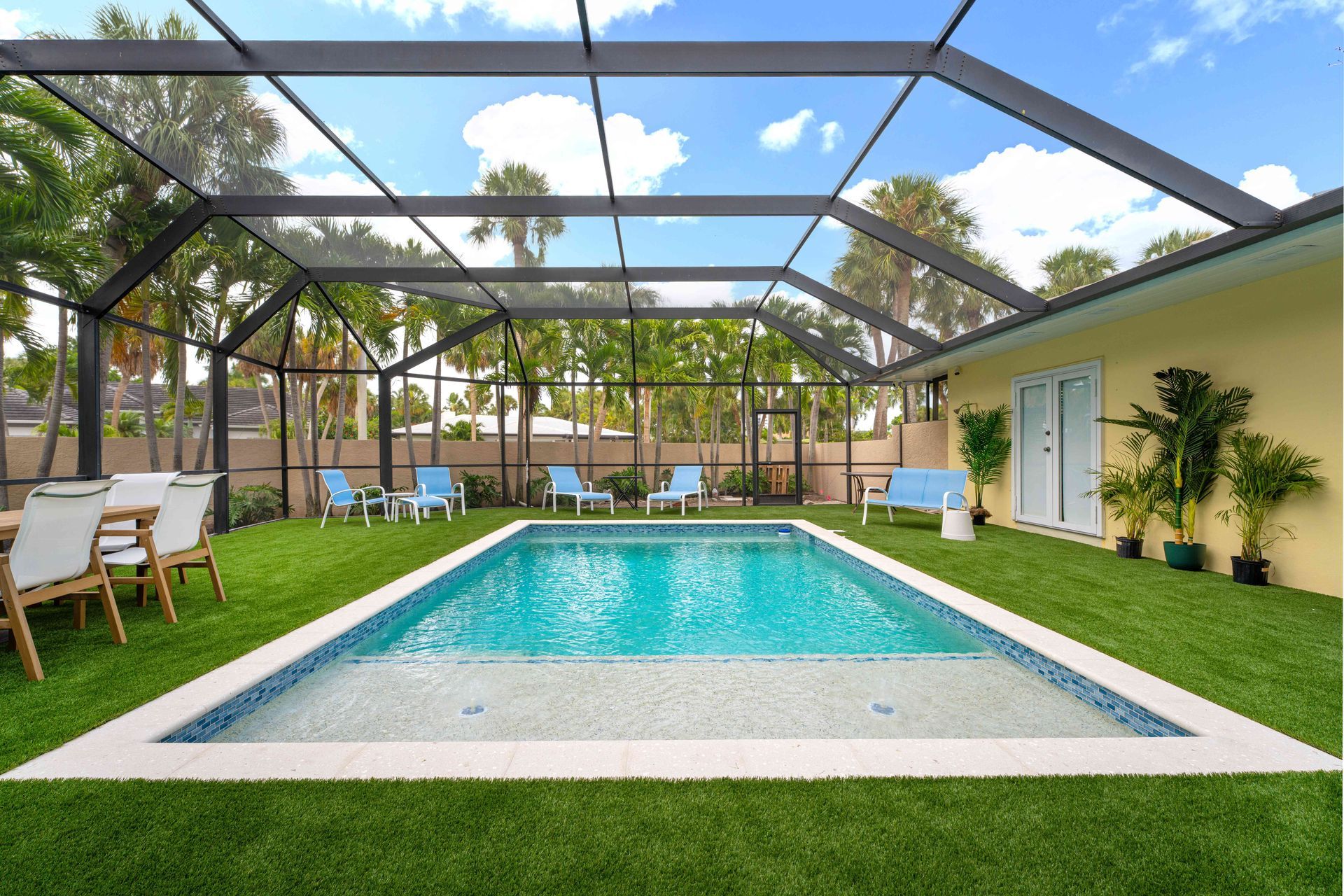 Covered backyard pool with turquoise water, lounge chairs, and a screened patio under blue sky.