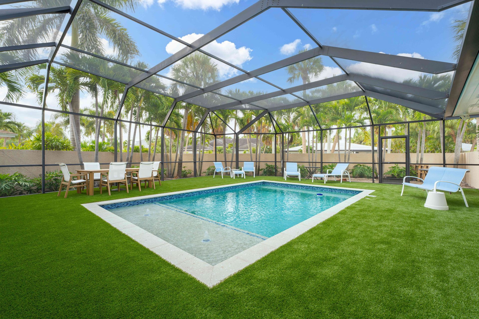 Screened-in backyard pool with turquoise water, bright green lawn, and lounge chairs under a blue sky.