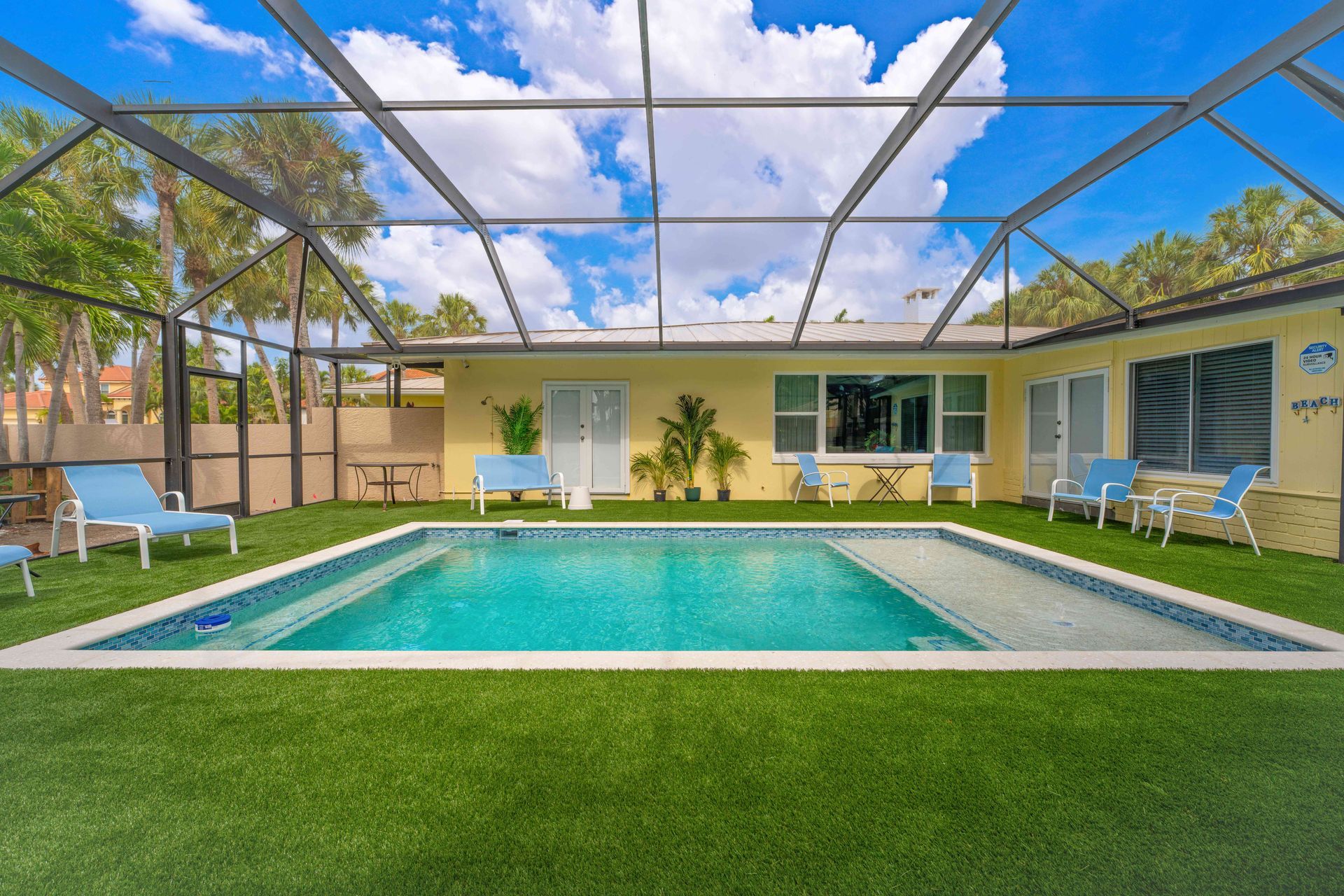 Screened backyard pool with turquoise water, lawn, and a beige house under a blue sky