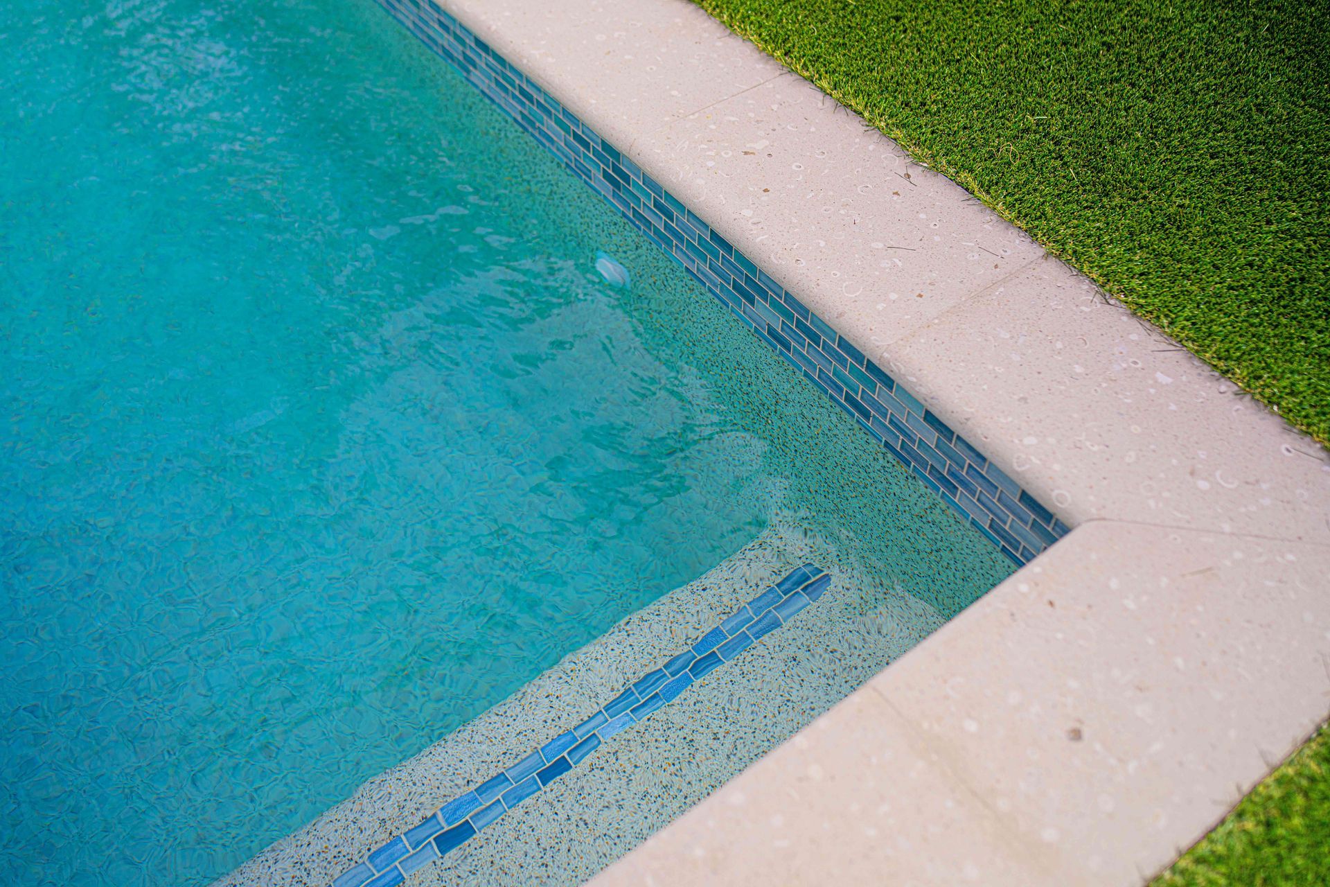 Turquoise swimming pool corner with white edge and green grass beside it
