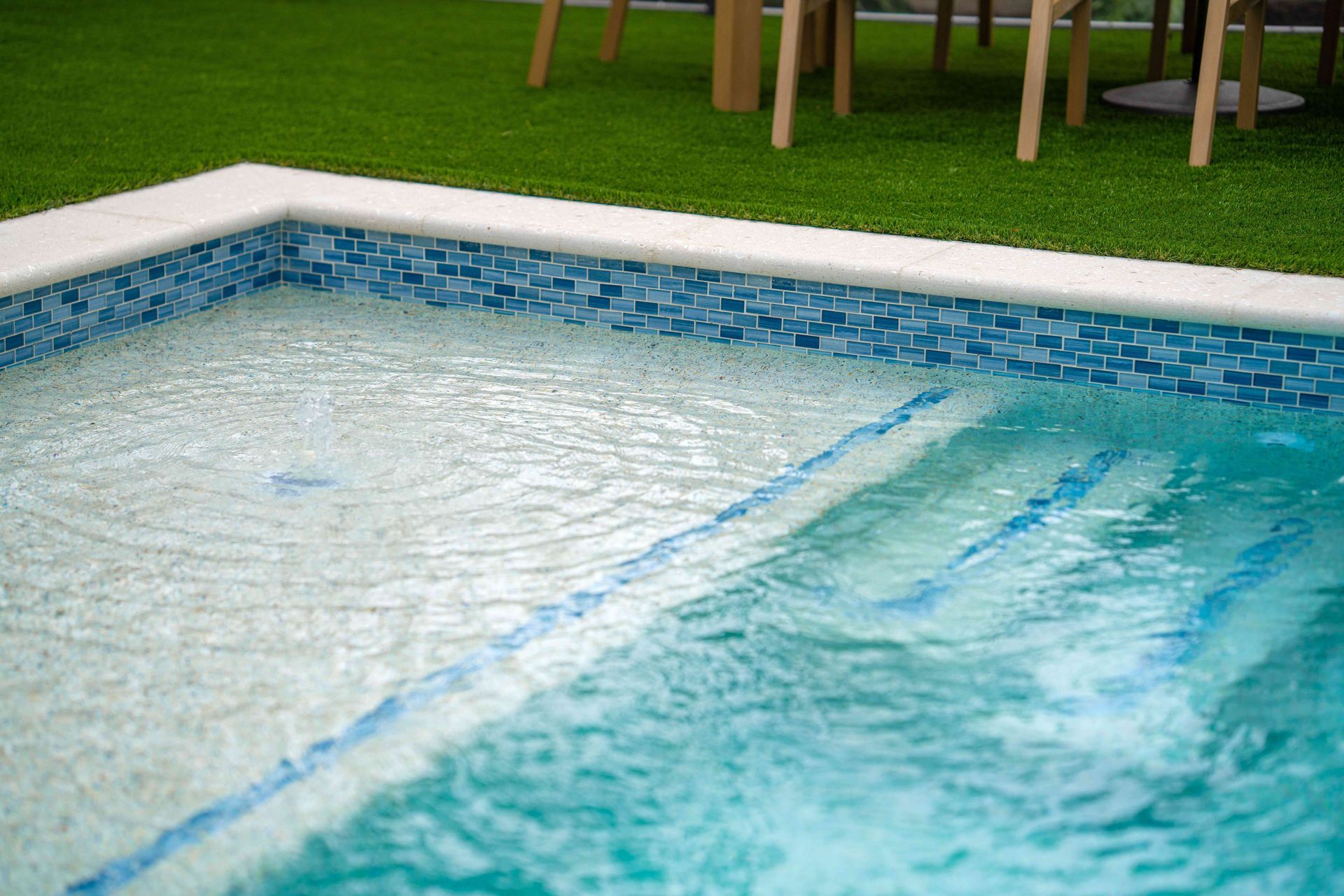 Swimming pool with clear blue water beside a grassy lawn and patio chairs