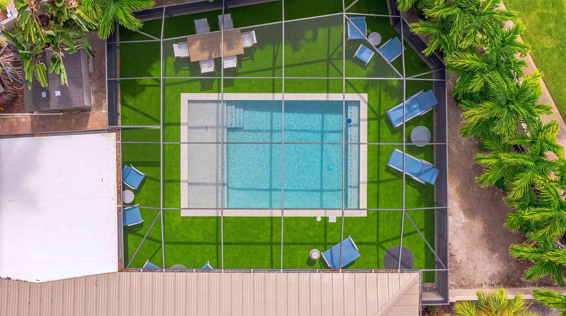 Top-down view of a small backyard pool with blue lounge chairs, green lawn, and stone patio