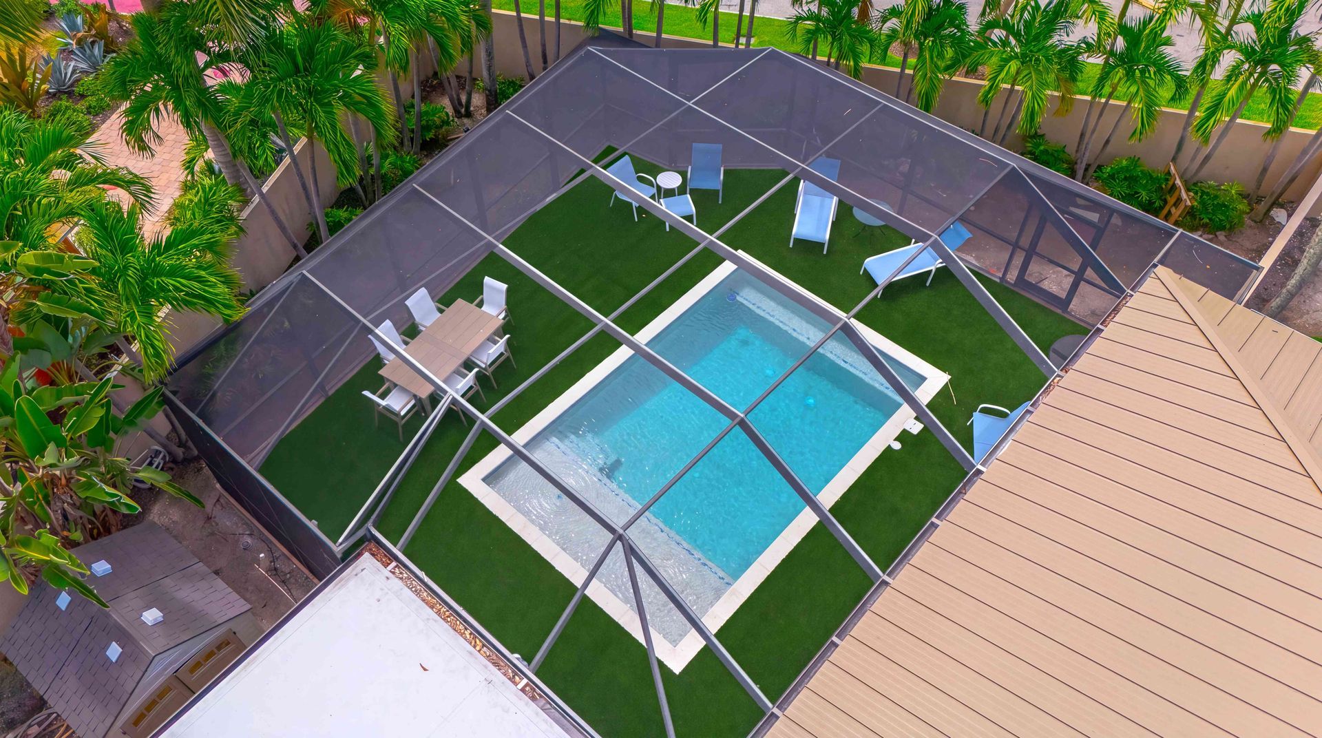 Aerial view of a fenced backyard pool with blue water, lounge chairs, and surrounding green turf.