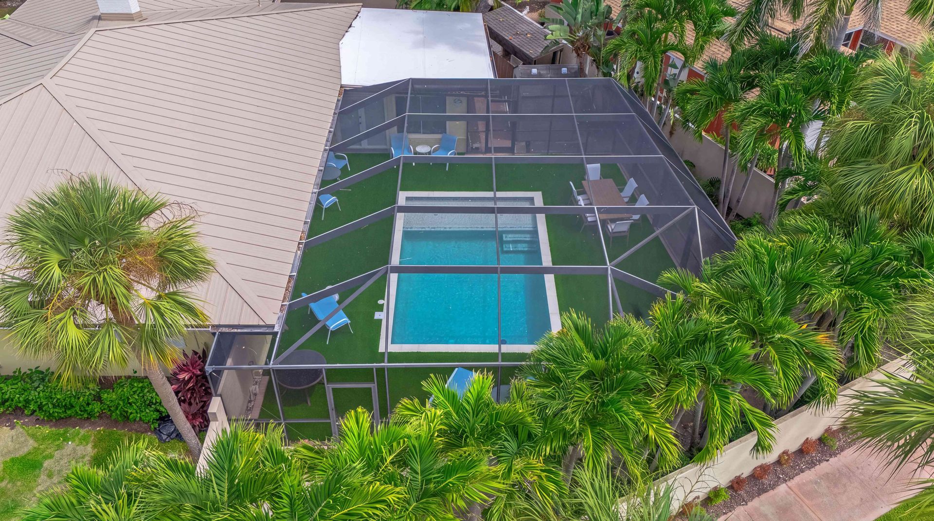 A screened backyard pool with turquoise water, surrounded by patio, trees, and a house roof from above