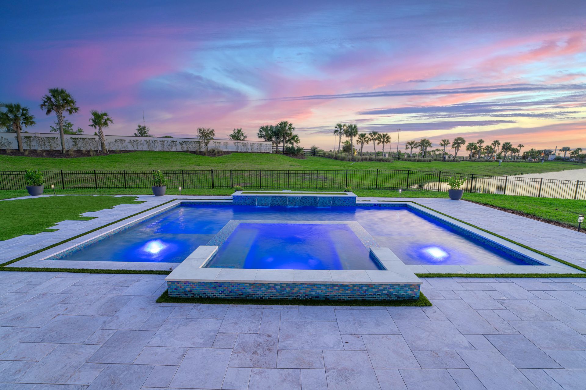 Modern backyard infinity pool glowing blue at sunset with palm trees and pastel sky