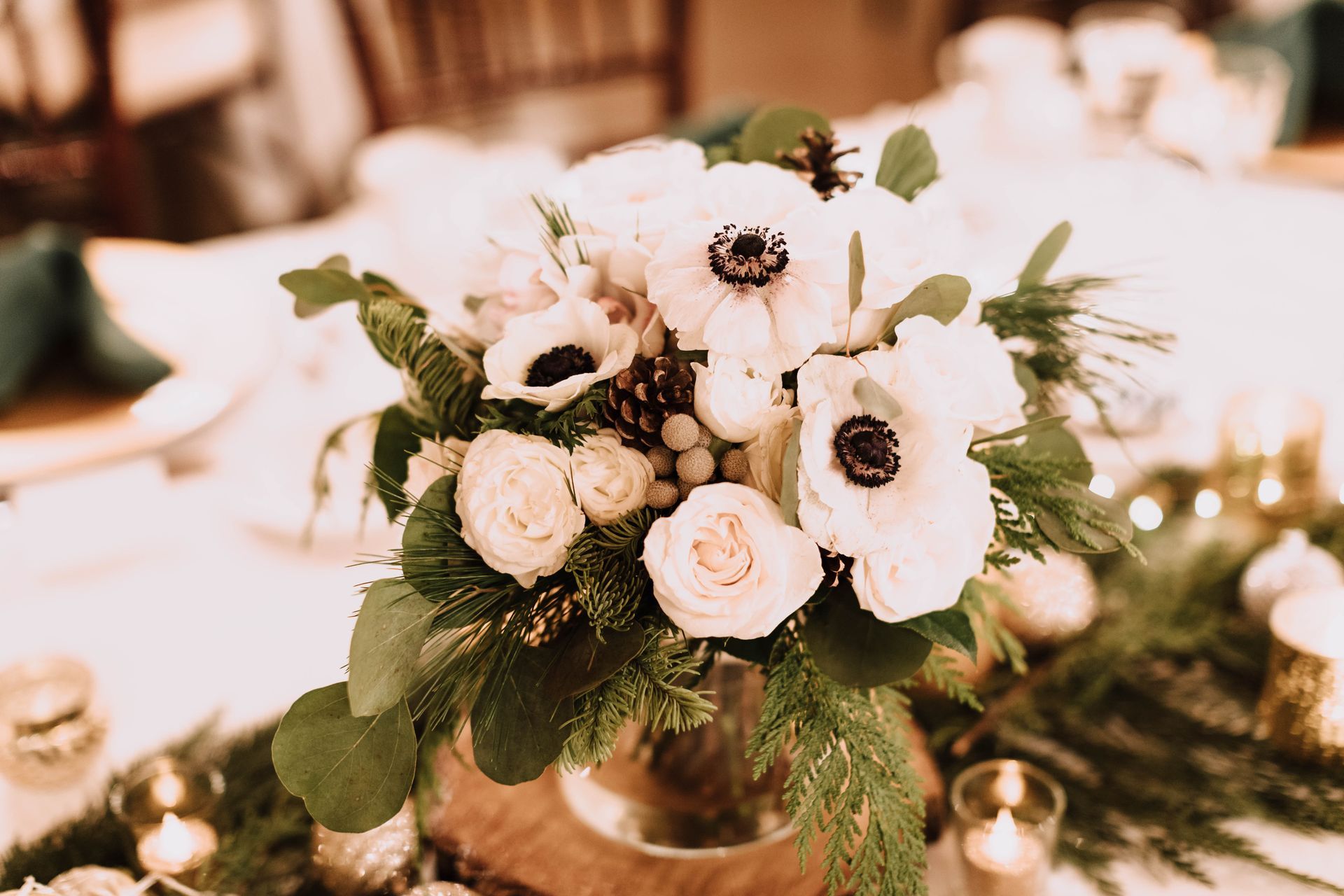 White floral centerpiece with anemones, roses, and greenery, on a decorated table with candles.