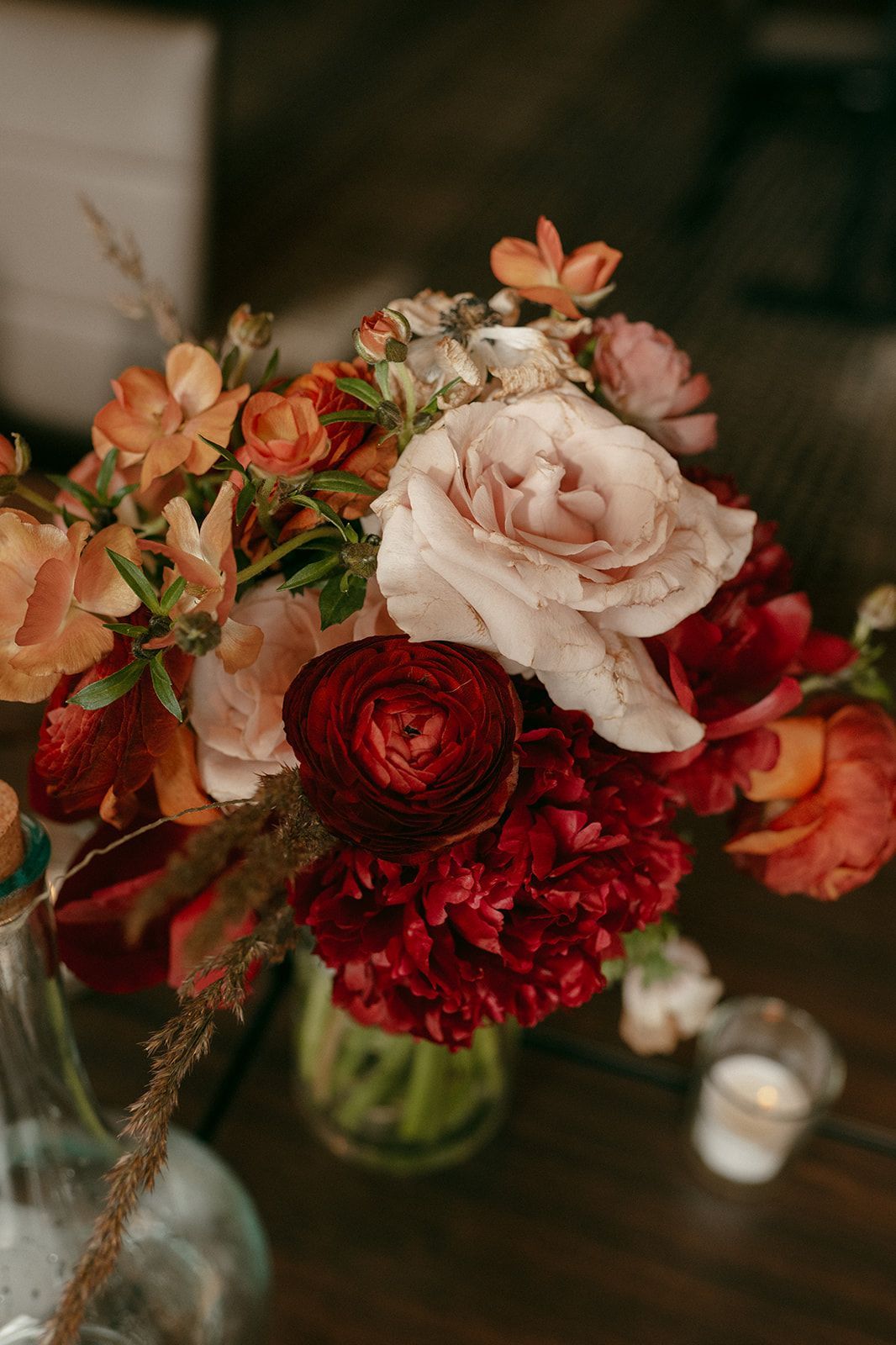 Floral bouquet with red, orange, and pink flowers in a glass vase on a wooden surface.