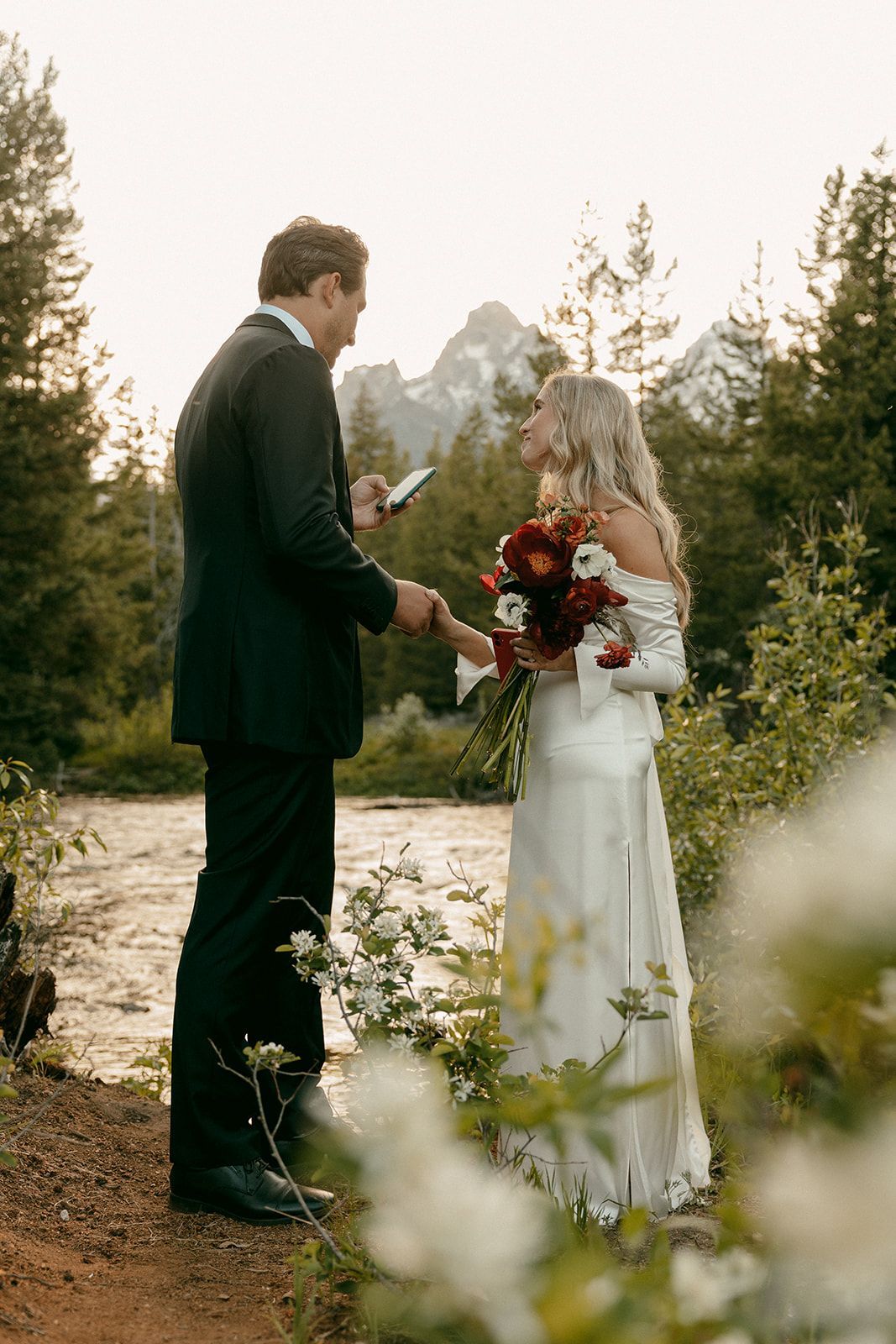 Bride and groom holding hands during outdoor wedding ceremony near a river.