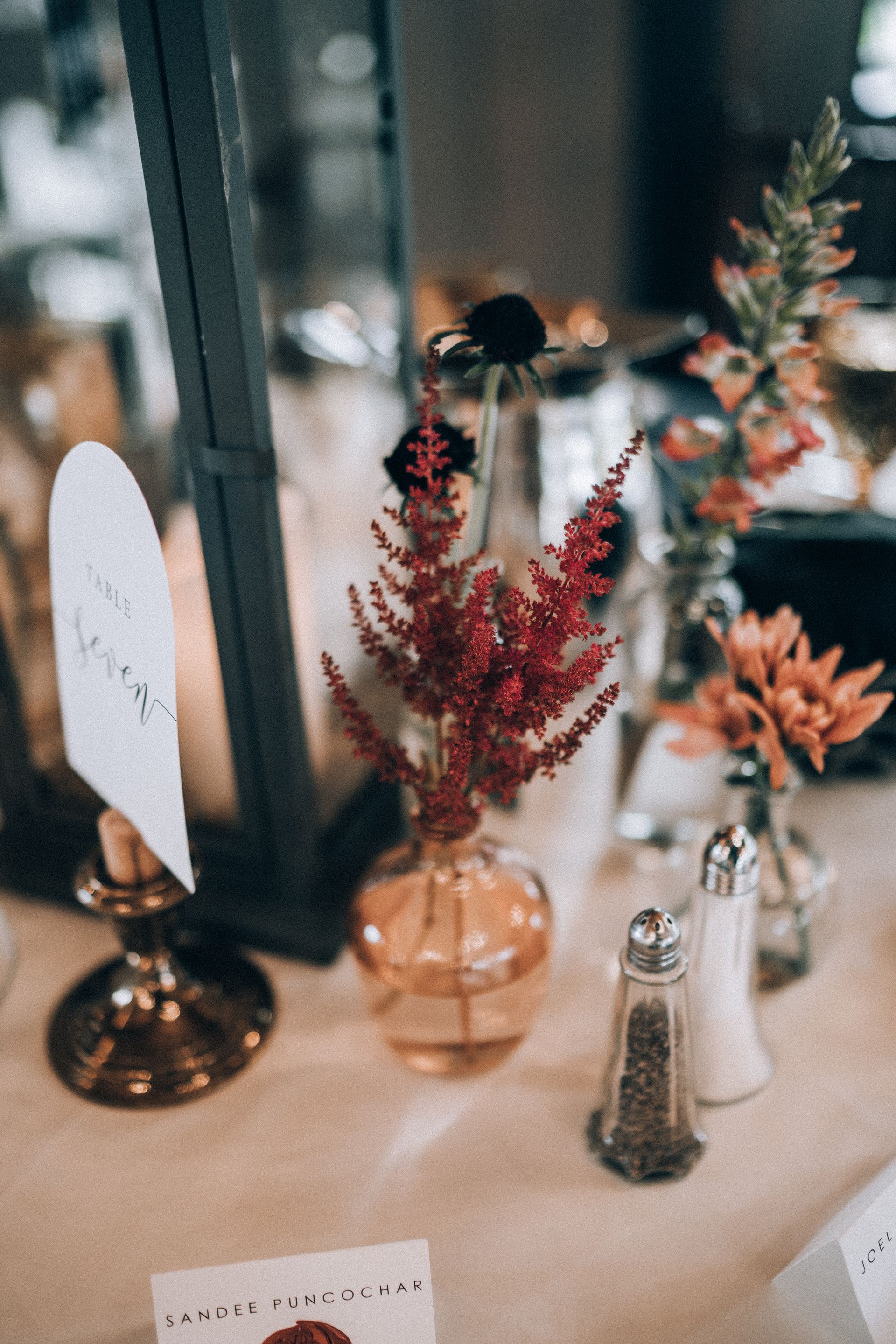 Floral table setting with red, orange, and black flowers in small glass vases, with salt and pepper shakers.