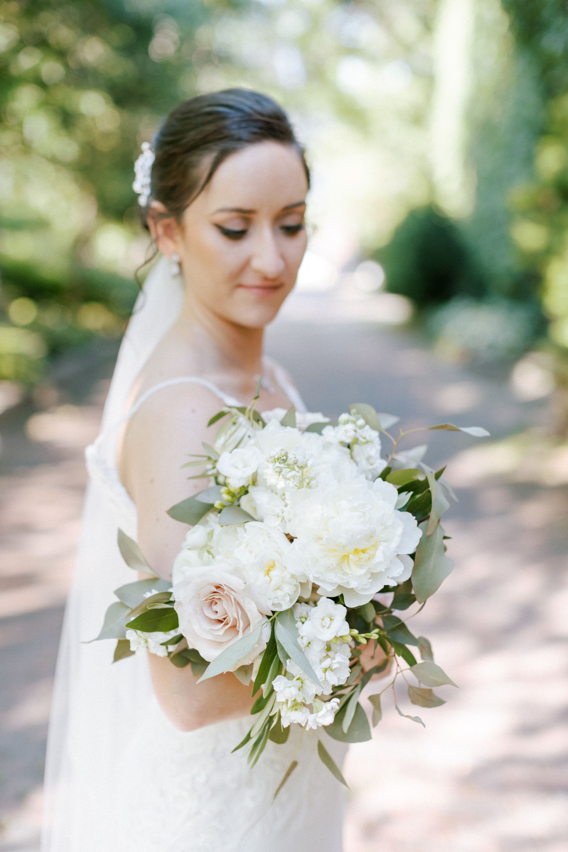 Bride holding a bouquet of white and pink flowers, wearing a veil, in an outdoor setting.