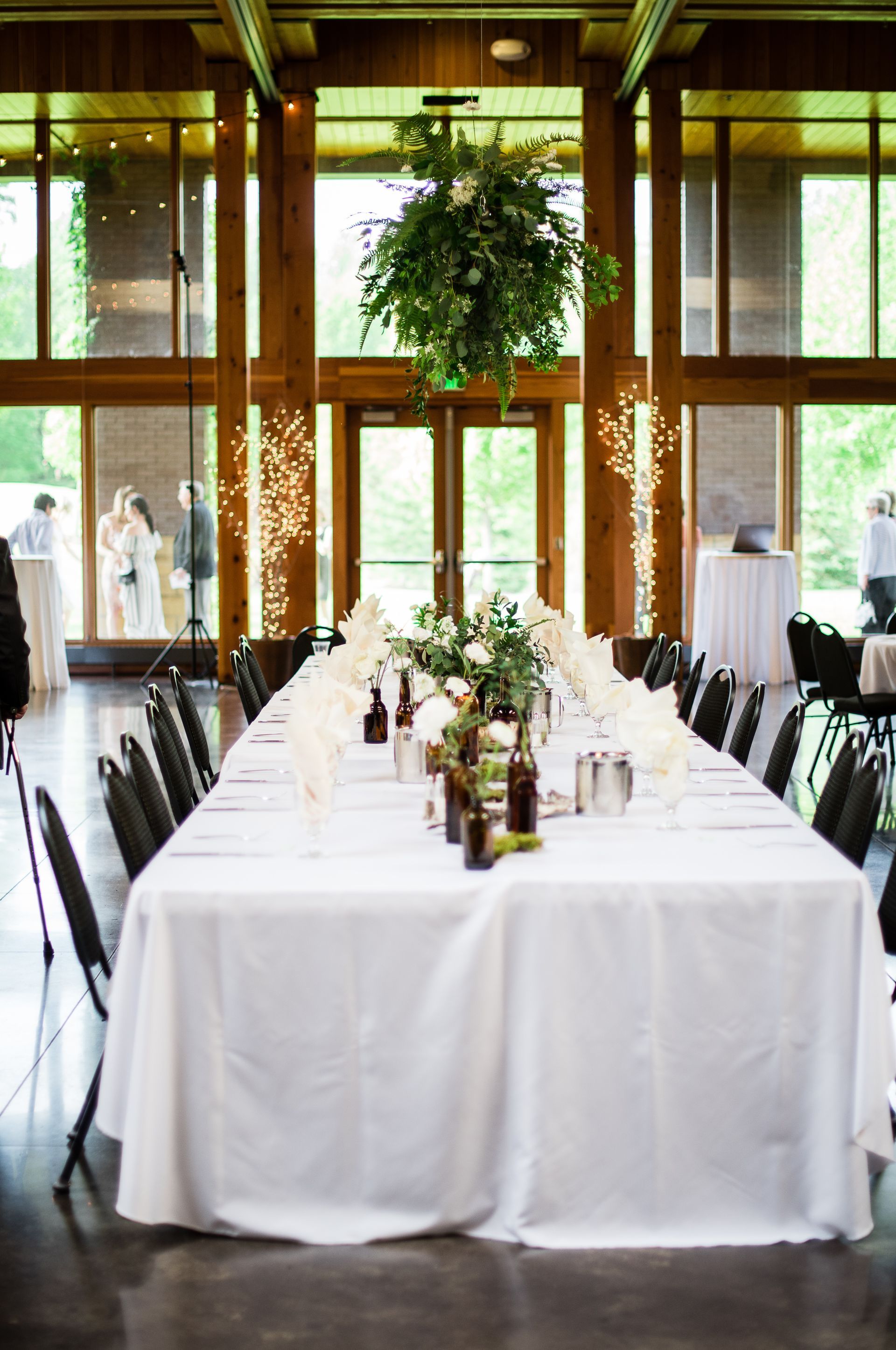 Long wedding reception table set with white linens; green floral chandelier.