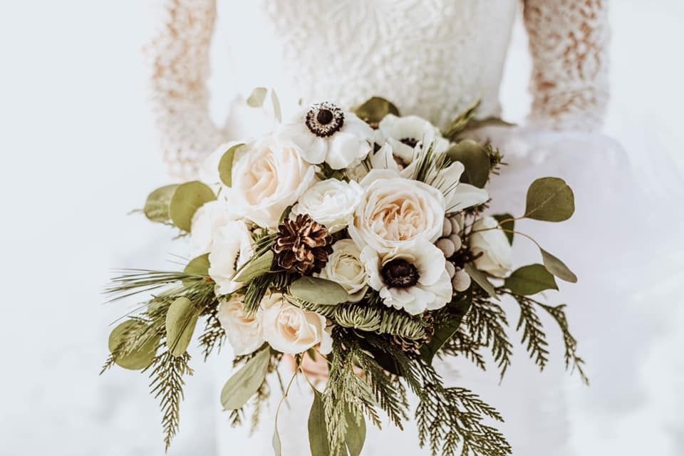 Bride in white dress holding a bouquet of cream roses, anemones, and greenery.
