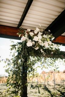 Floral arrangement of white roses and green foliage on a wooden arbor, outdoors.