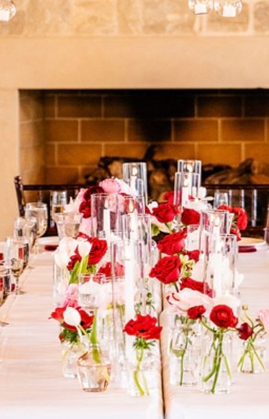 Table setting with red and white flowers in glass vases, fireplace in the background.