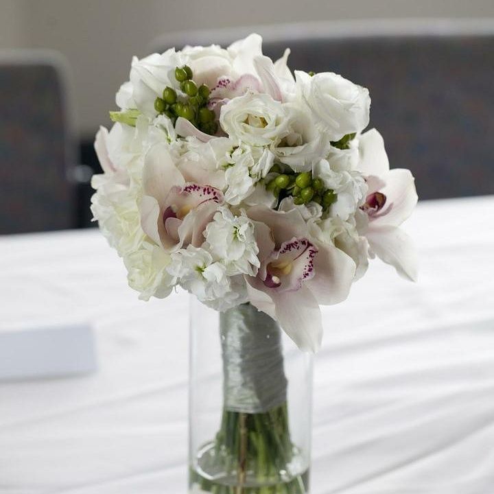 White and blush floral bouquet in a clear vase, on a white tablecloth.