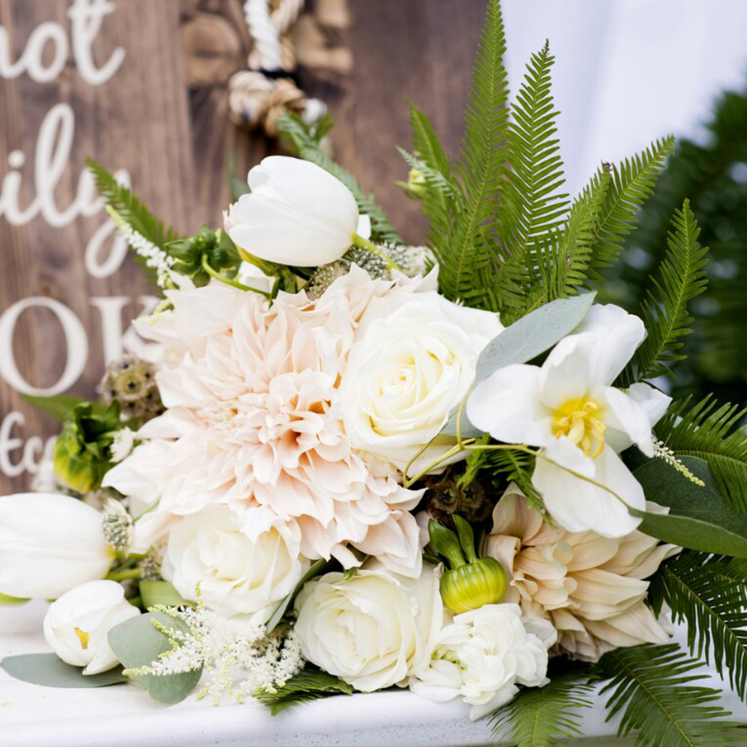 Wedding bouquet with cream roses, dahlias, and white tulips, with ferns.