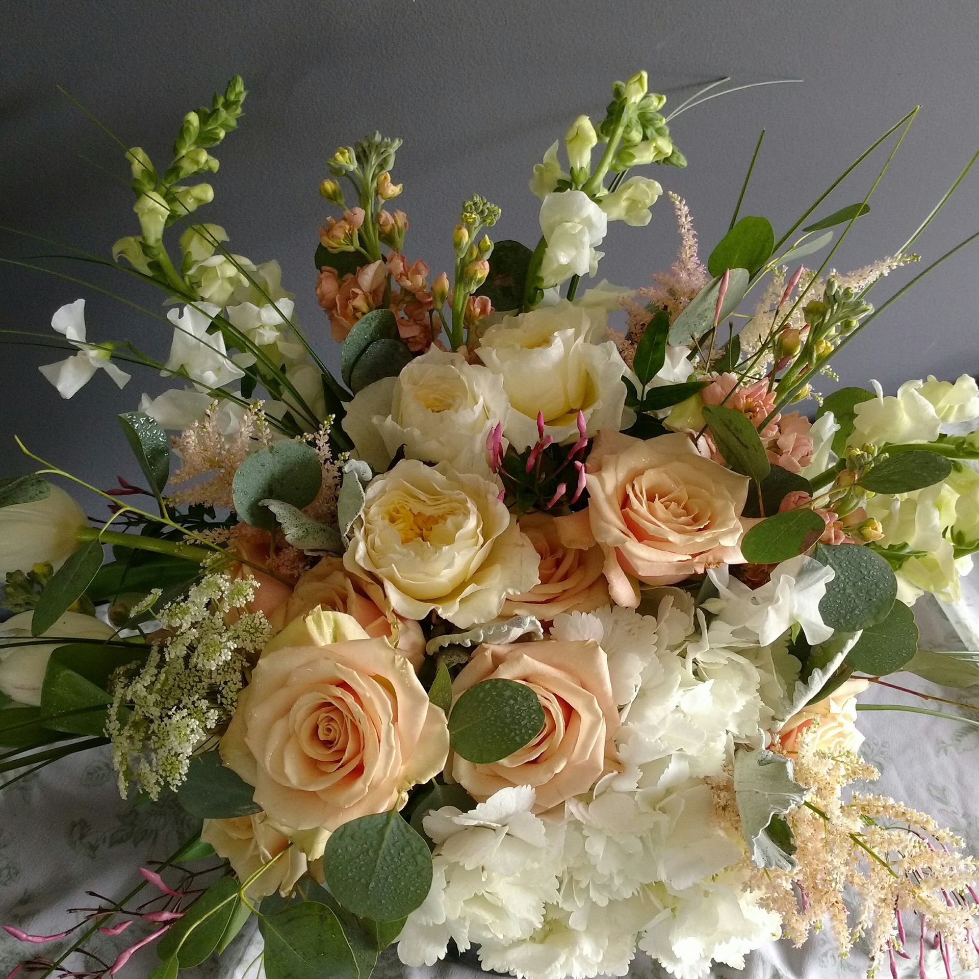 Close-up of a floral arrangement with peach roses, white hydrangeas, and greenery.