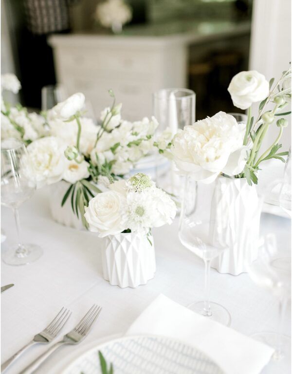 White floral centerpiece on a table set for a wedding with white flowers, glasses, and silverware.