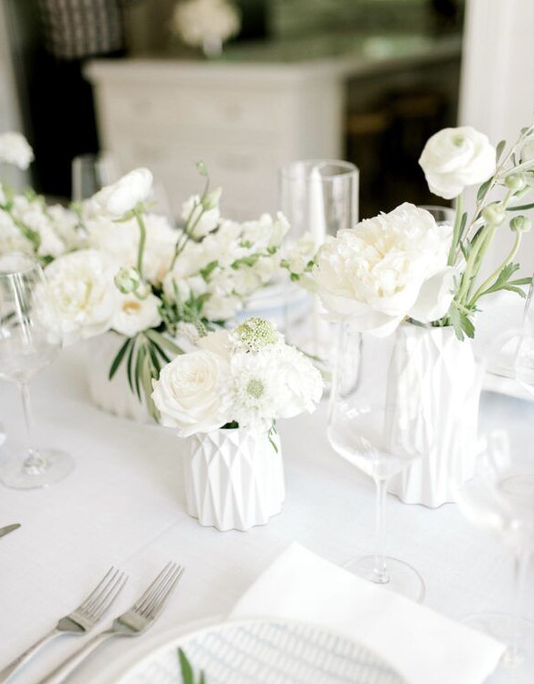 White floral centerpiece on a table set for a wedding with white flowers, glasses, and silverware.