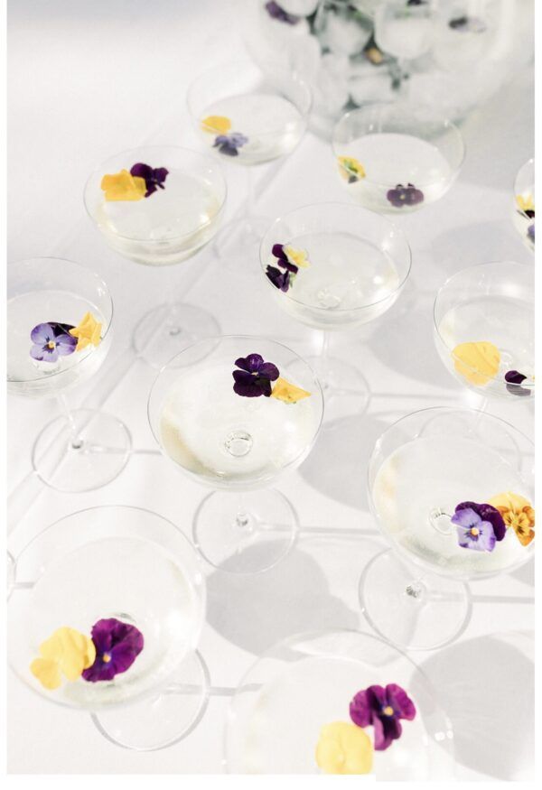 Champagne flutes with edible flowers, on a white surface, bright lighting.