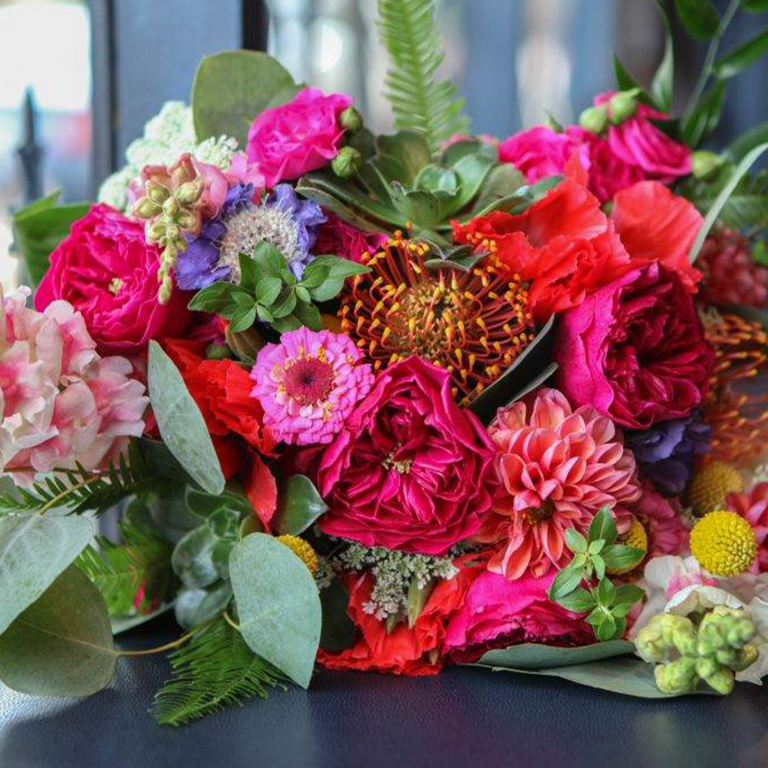Colorful bouquet of flowers on a blue surface, including roses, dahlias, and succulents.