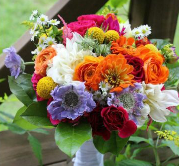 Colorful bouquet of flowers: orange, pink, white, yellow, red, purple. Green leaves and white wrap.