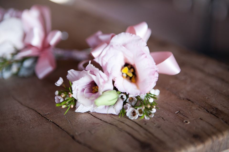 Close-up of pink floral wrist corsage with ribbon on wooden surface.