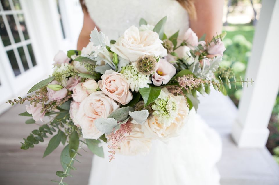 Bride holding a pastel bouquet of roses and greenery on a porch.