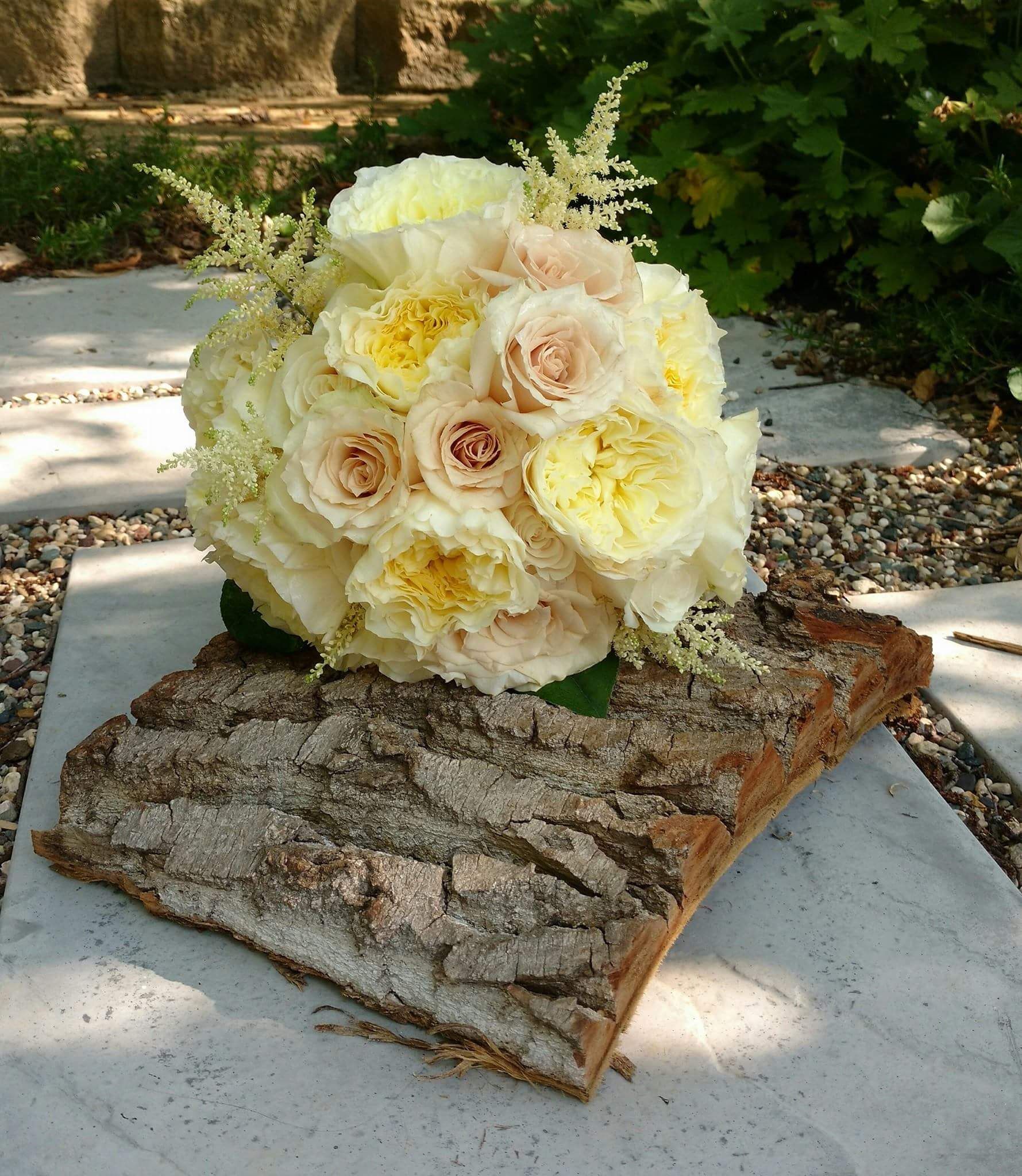 Wedding bouquet of cream and pale yellow roses on a piece of tree bark.