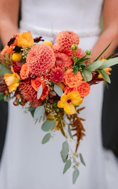 Bride holding vibrant orange and yellow floral bouquet.
