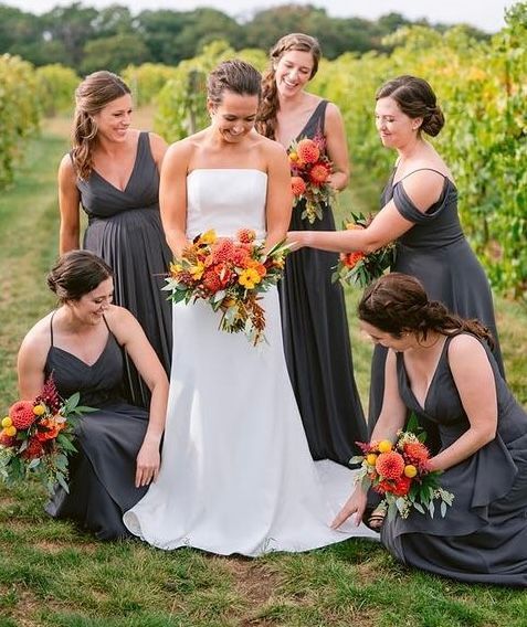Bride with bridesmaids in vineyard. Bride in white dress, bridesmaids in gray. All hold colorful bouquets.