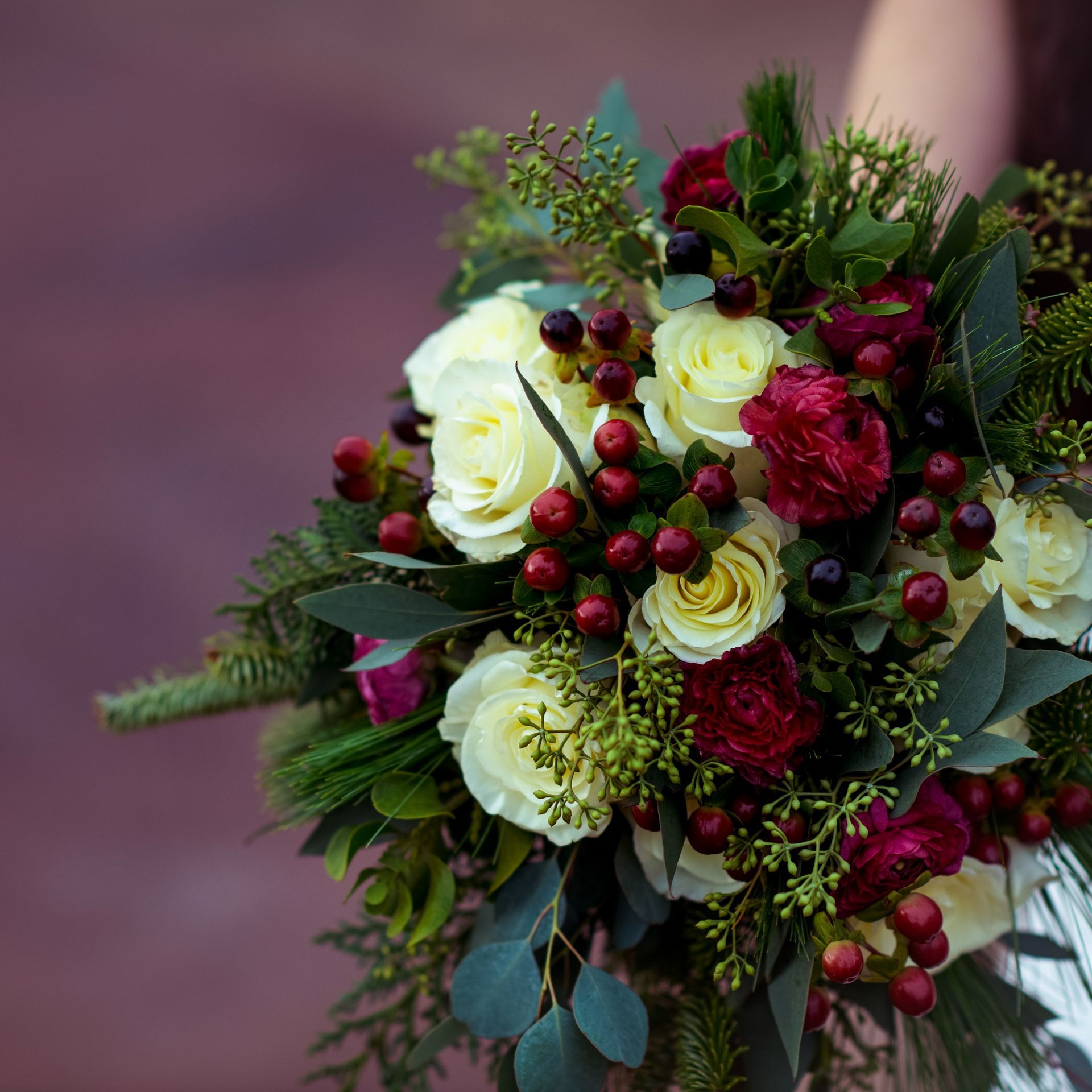 Bouquet of white and red roses with red berries and green foliage.
