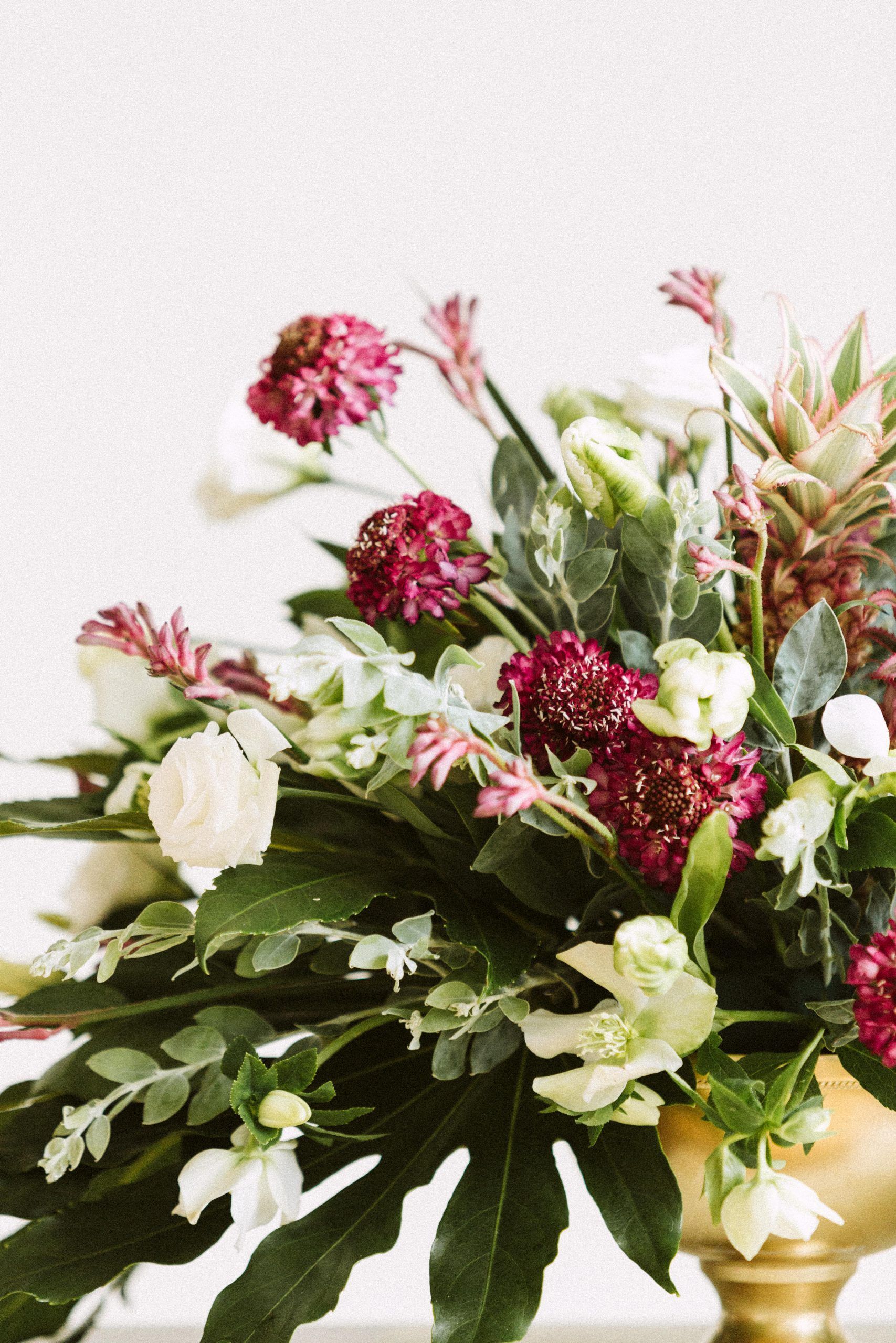 Floral arrangement with burgundy and white blooms in a gold vase.