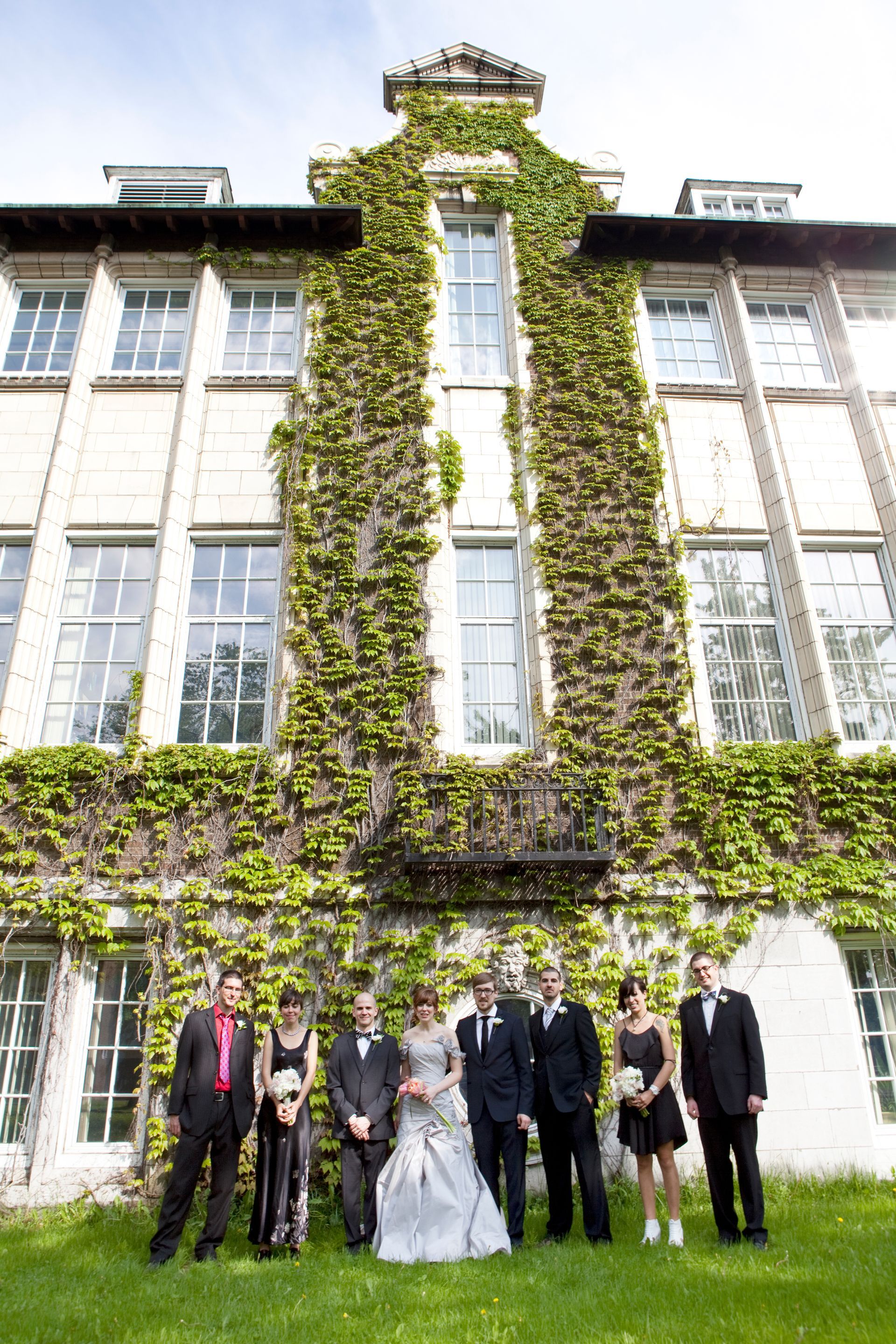 Wedding party posing in front of ivy-covered building with multiple windows.