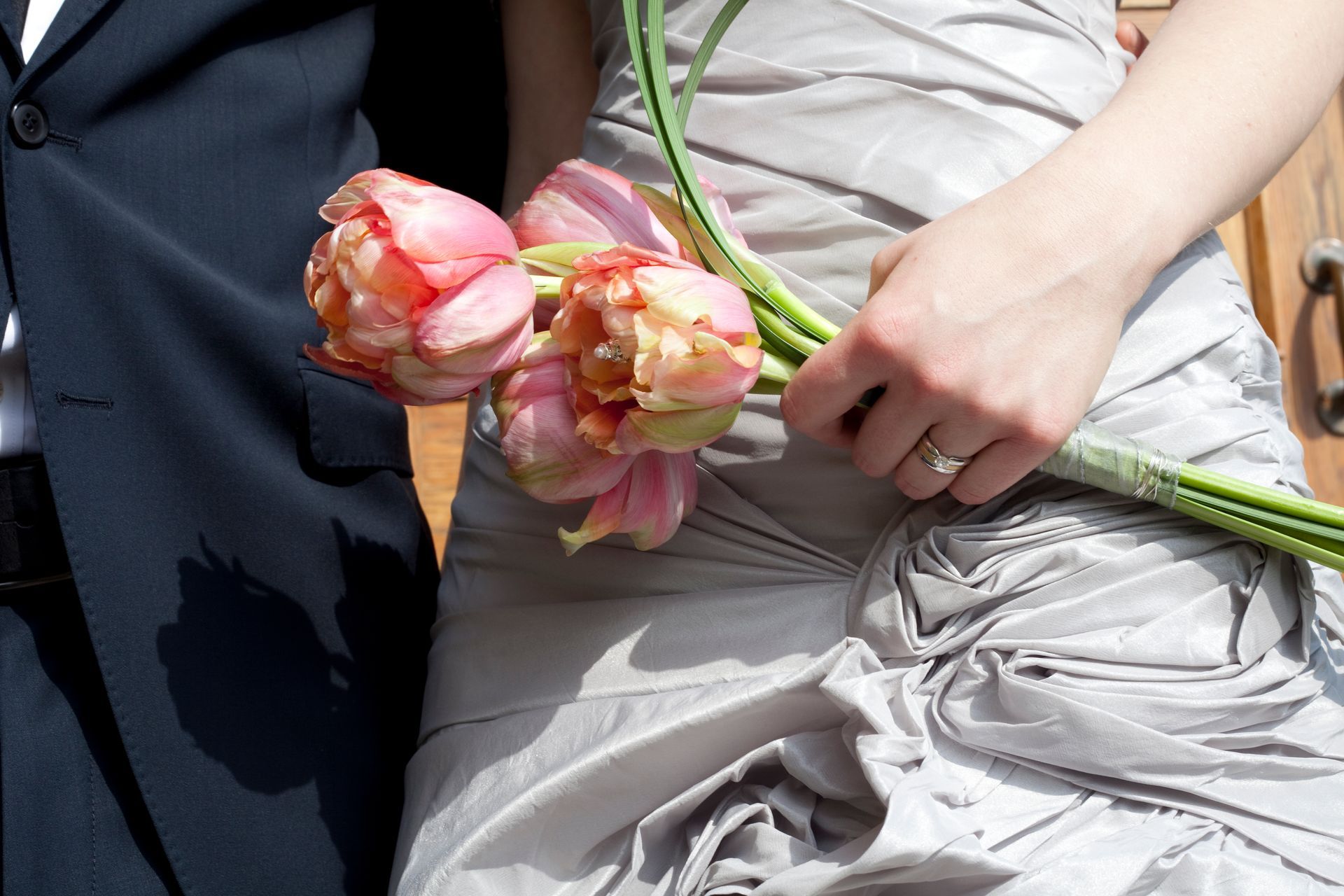 Person in a gray dress holding a bouquet of pink and yellow tulips next to someone wearing a suit.