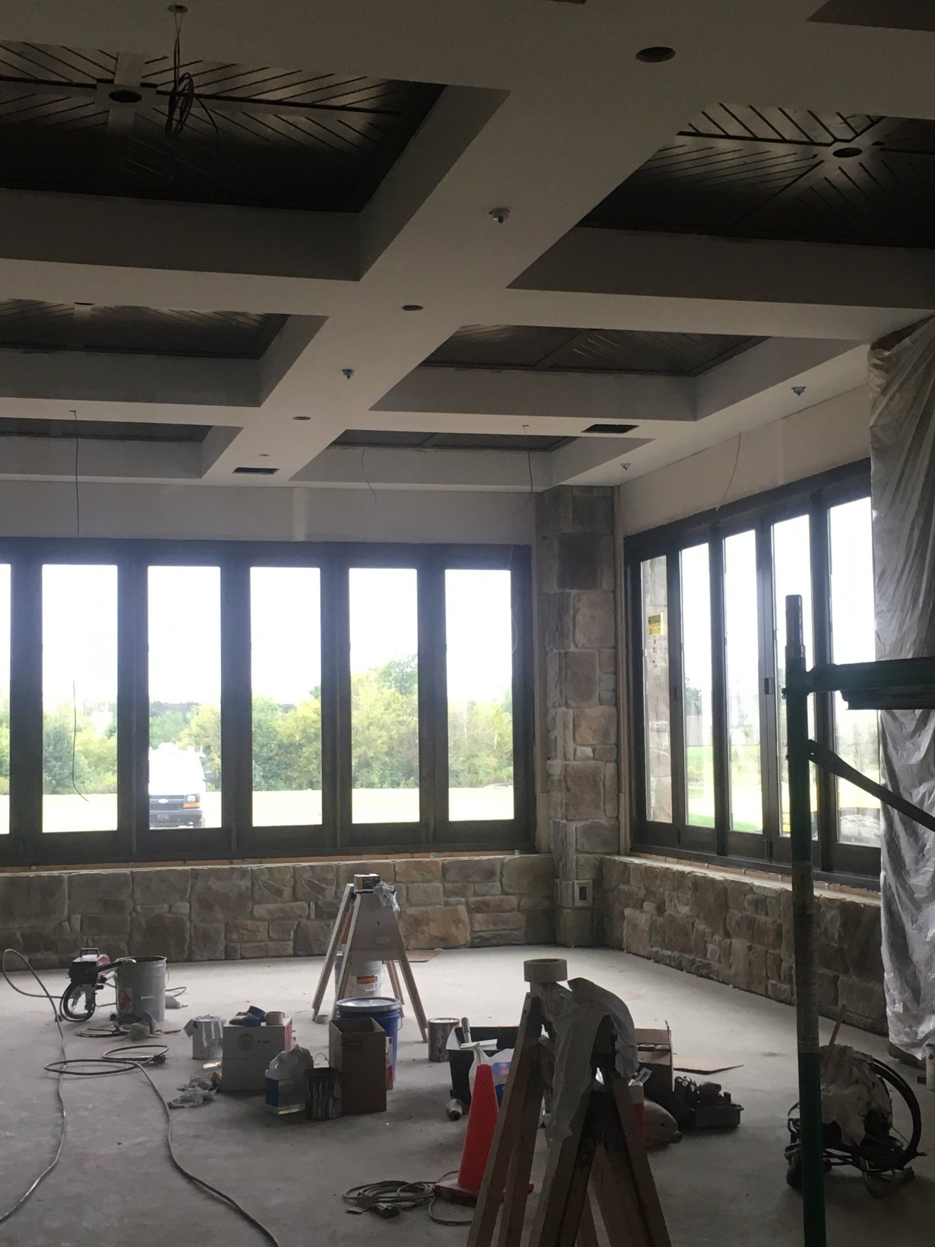 Unfinished room with large windows, exposed ceiling, and construction tools on the floor.