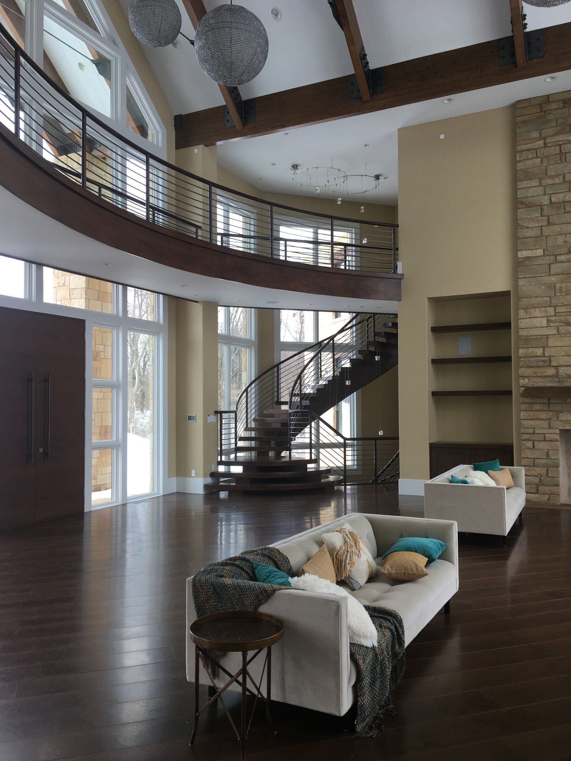 Spacious modern living room with tall windows, spiral staircase, white sofas, and dark wood floors