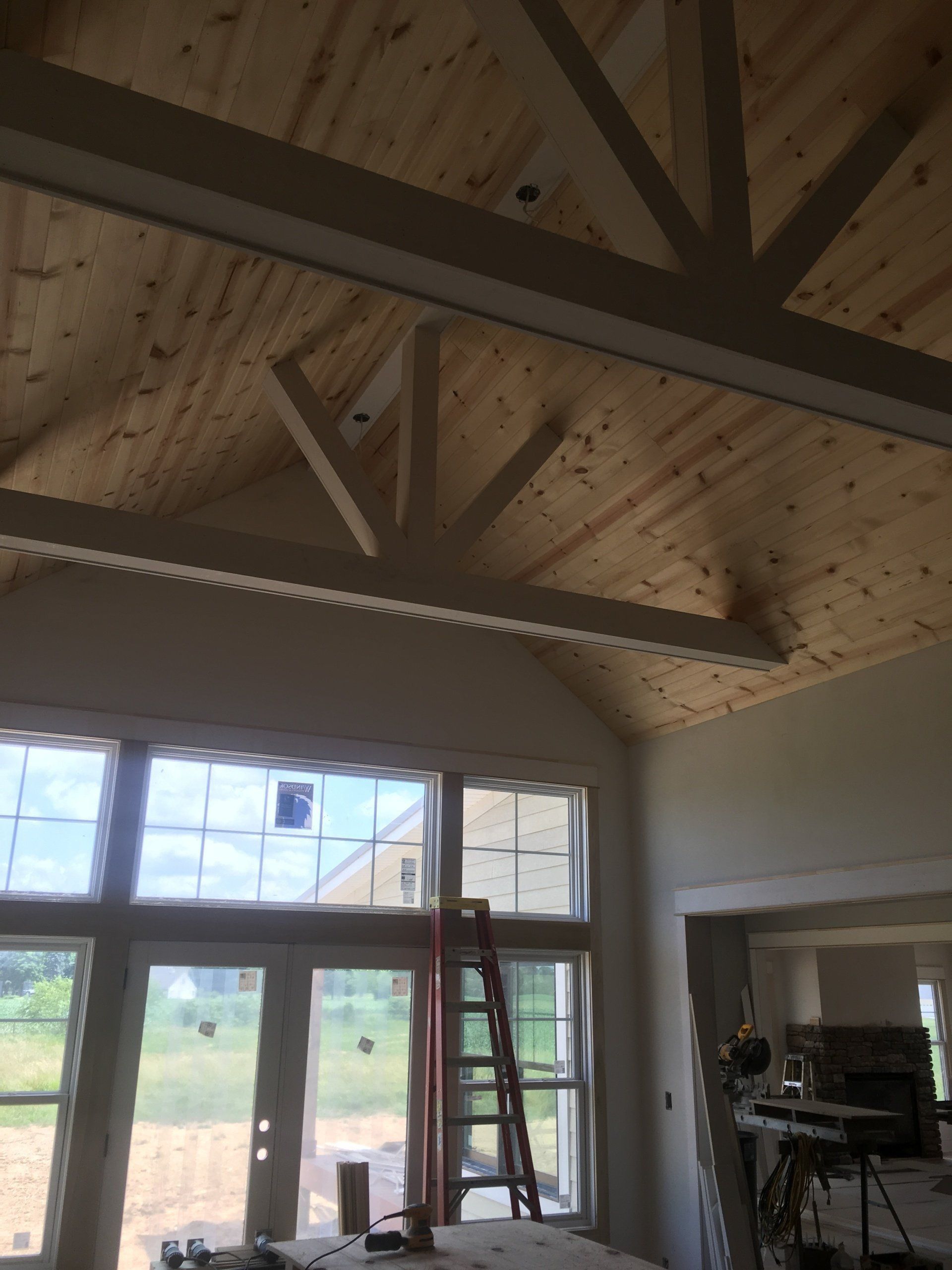 Interior room with exposed wooden ceiling beams, large windows, and a ladder near a doorway.