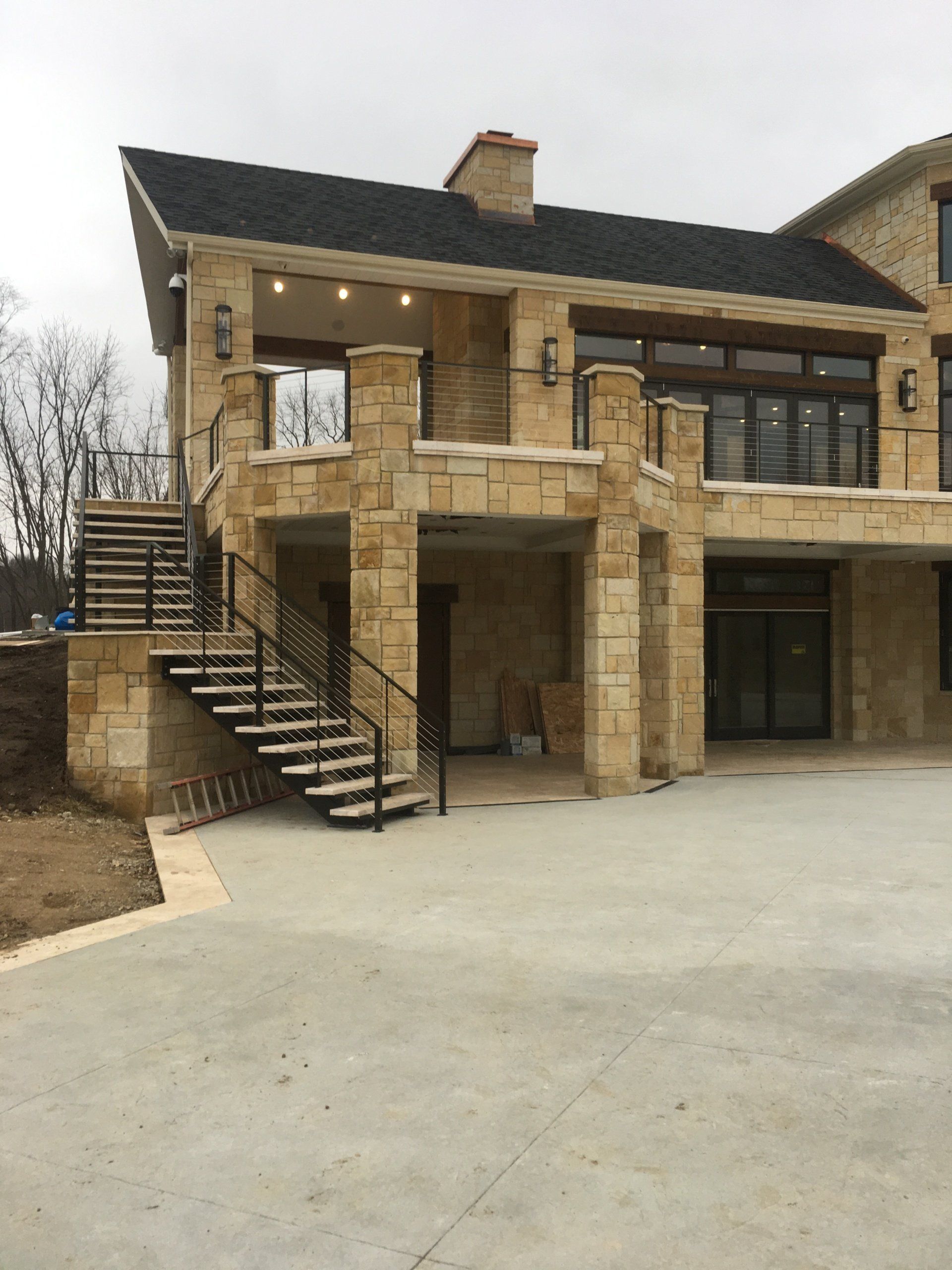 Stone house exterior with black roof, balcony, and outdoor staircase leading to a covered entry