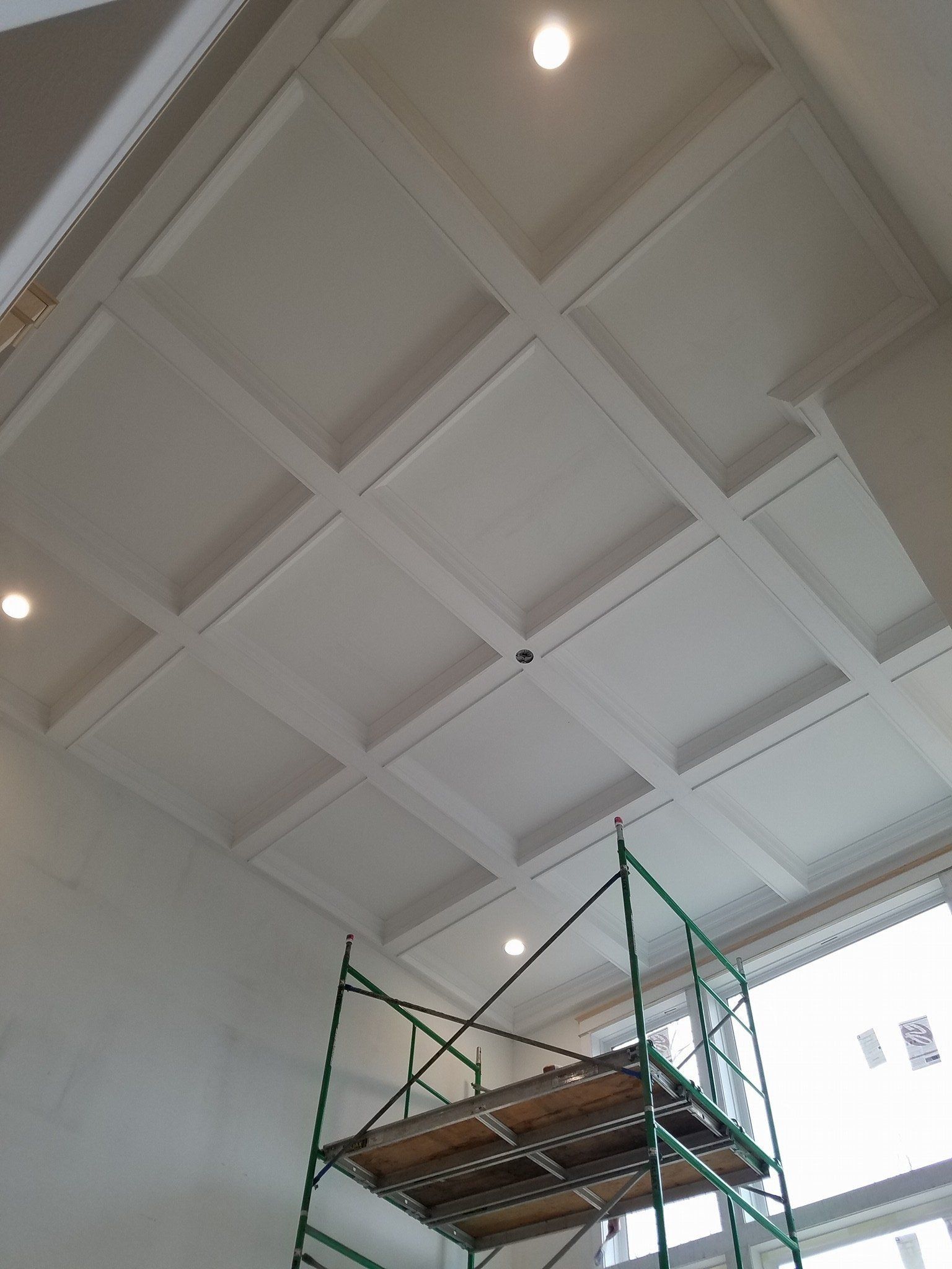 Scaffolding under a white coffered ceiling with recessed lights in a tall room