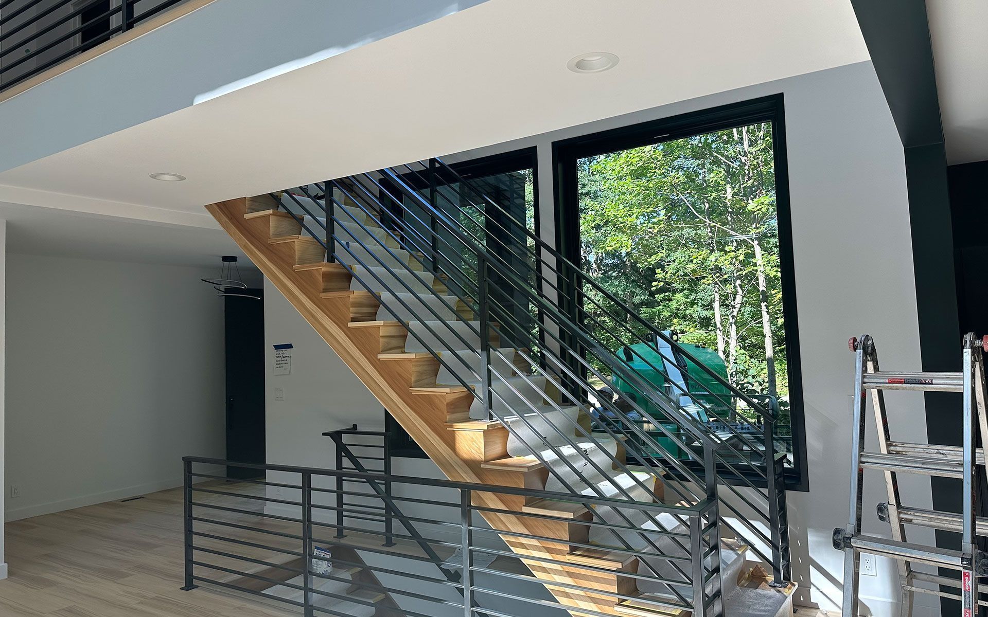 Modern interior staircase with wood steps, black railing, and large windows overlooking trees