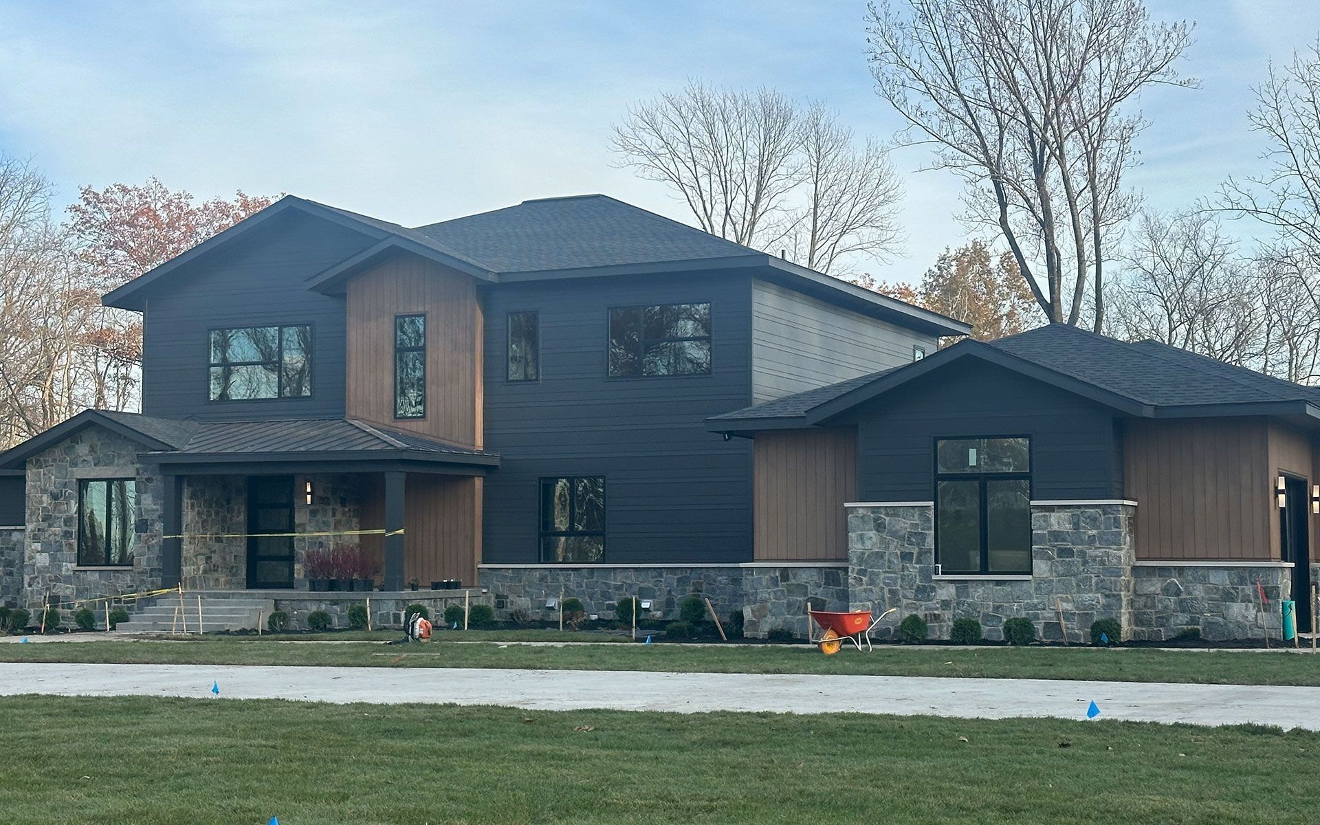 Large modern two-story house with dark siding, stone accents, and a front lawn under bare trees