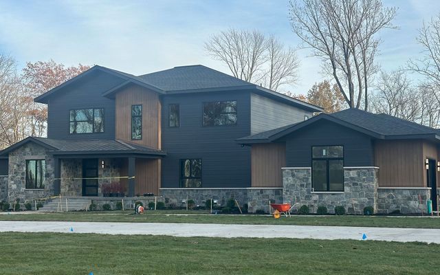 Large modern two-story house with dark siding, stone accents, and a front lawn under bare trees