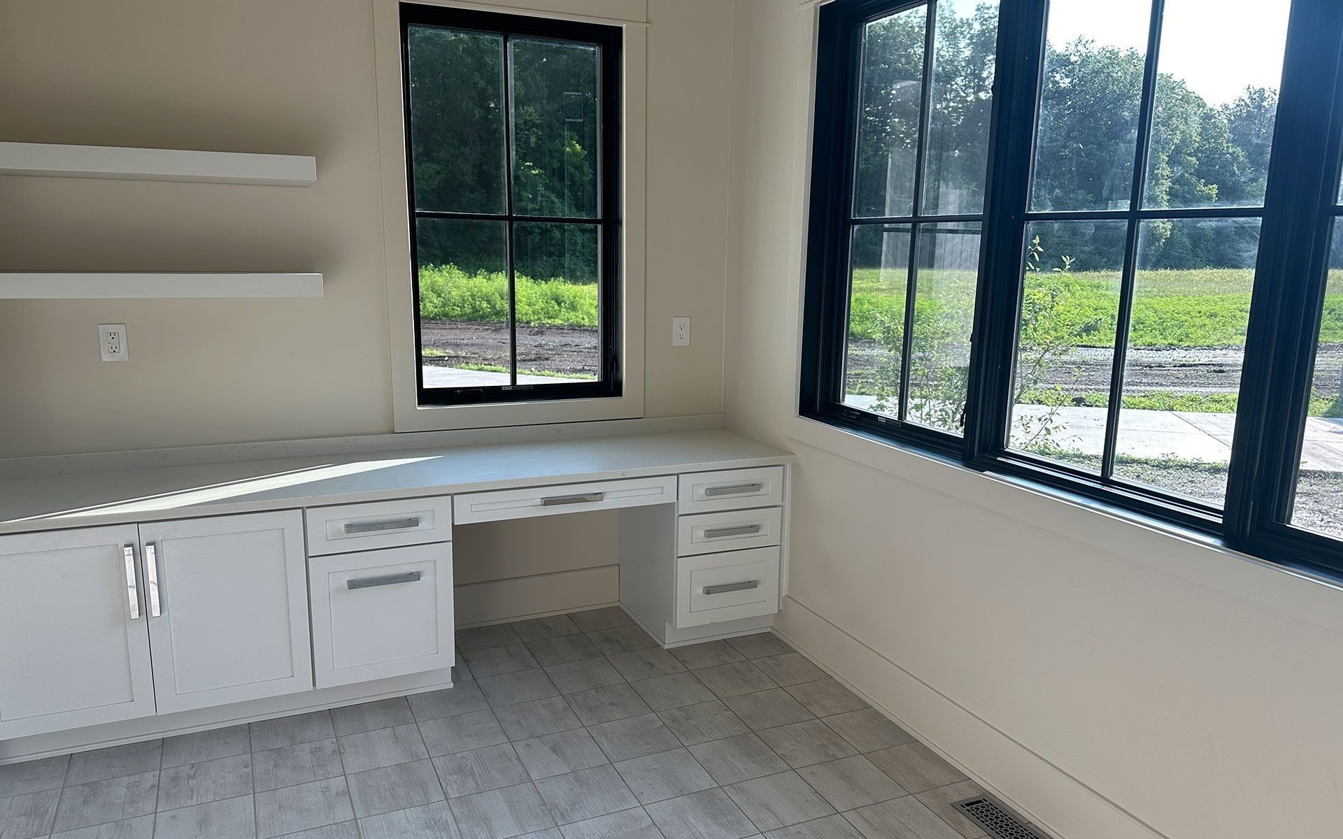 Empty office with white cabinets, desk, and large black-framed windows overlooking greenery.