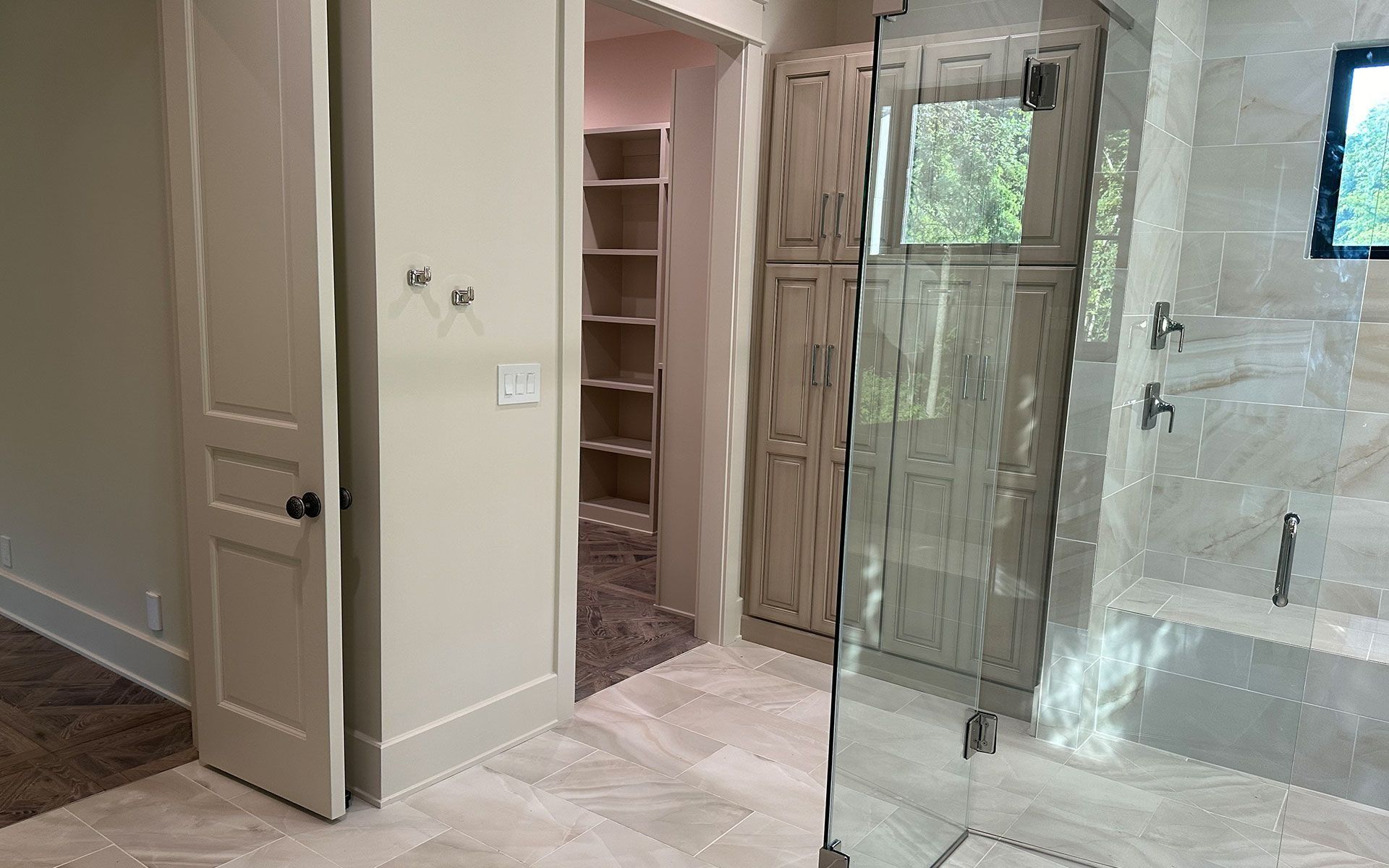 Bathroom with glass shower enclosure, tiled floor, and built-in shelving beside a doorway