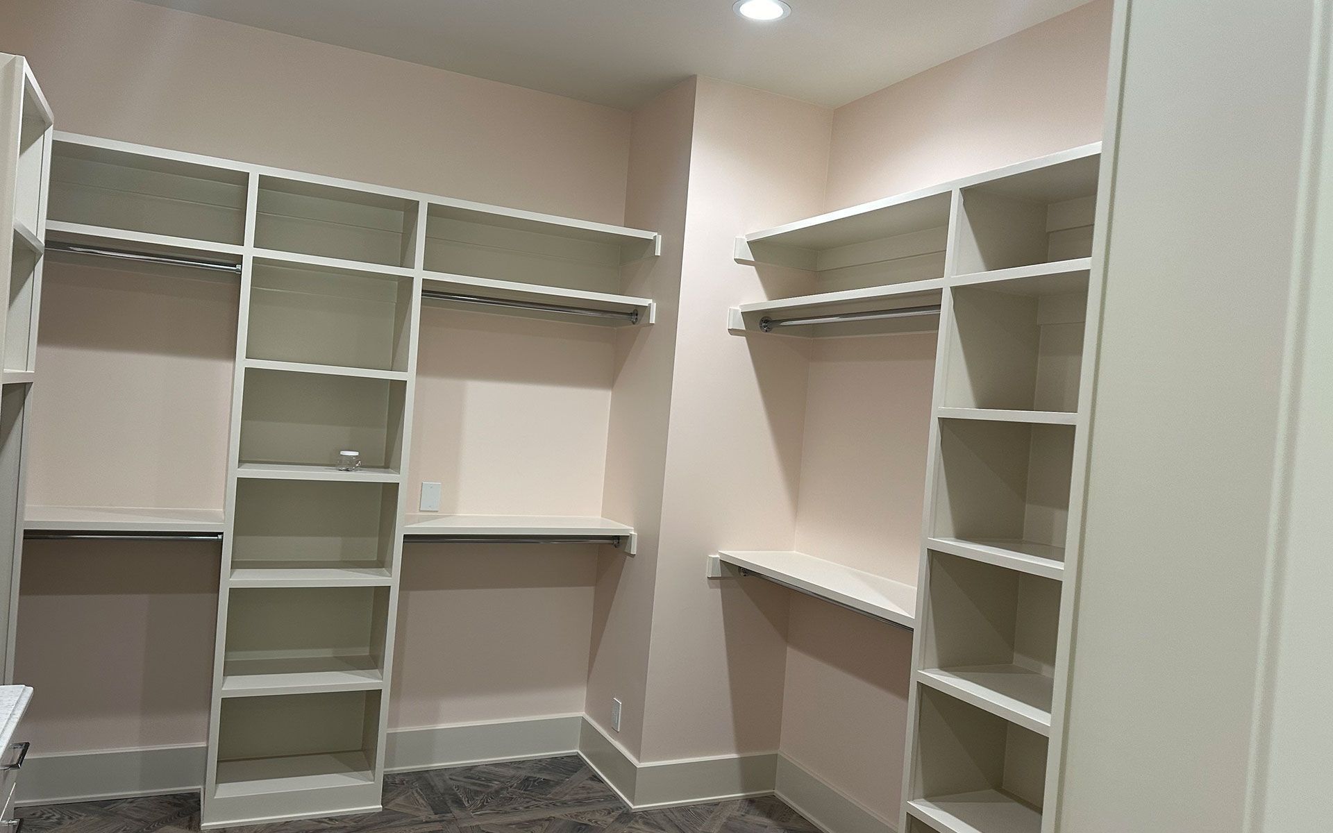 Walk-in closet with white built-in shelves, hanging rods, and beige walls
