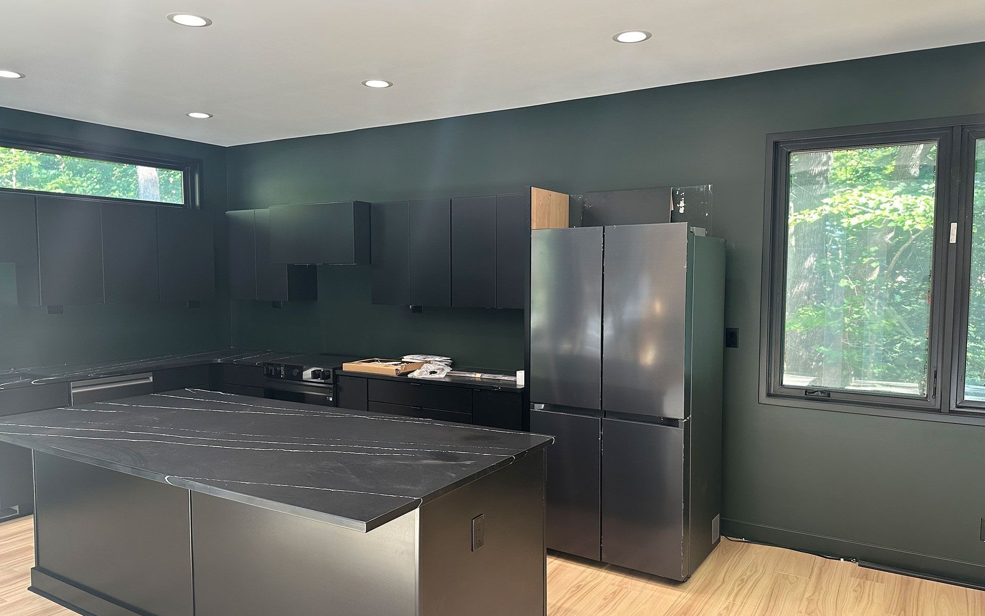 Modern kitchen with dark cabinets, black island, stainless refrigerator, and two windows