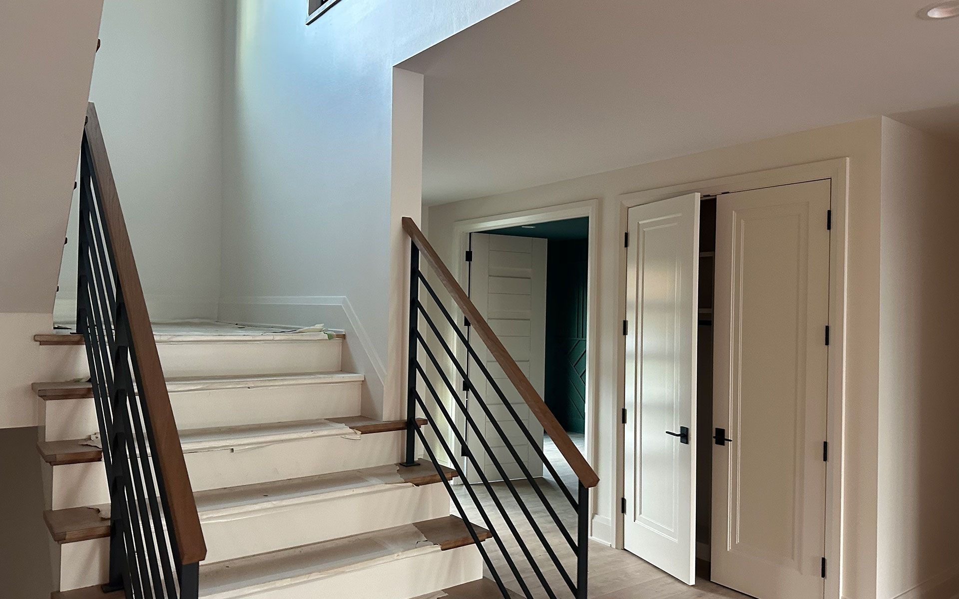 Interior staircase with white steps, black railing, and hallway doors in a bright home interior